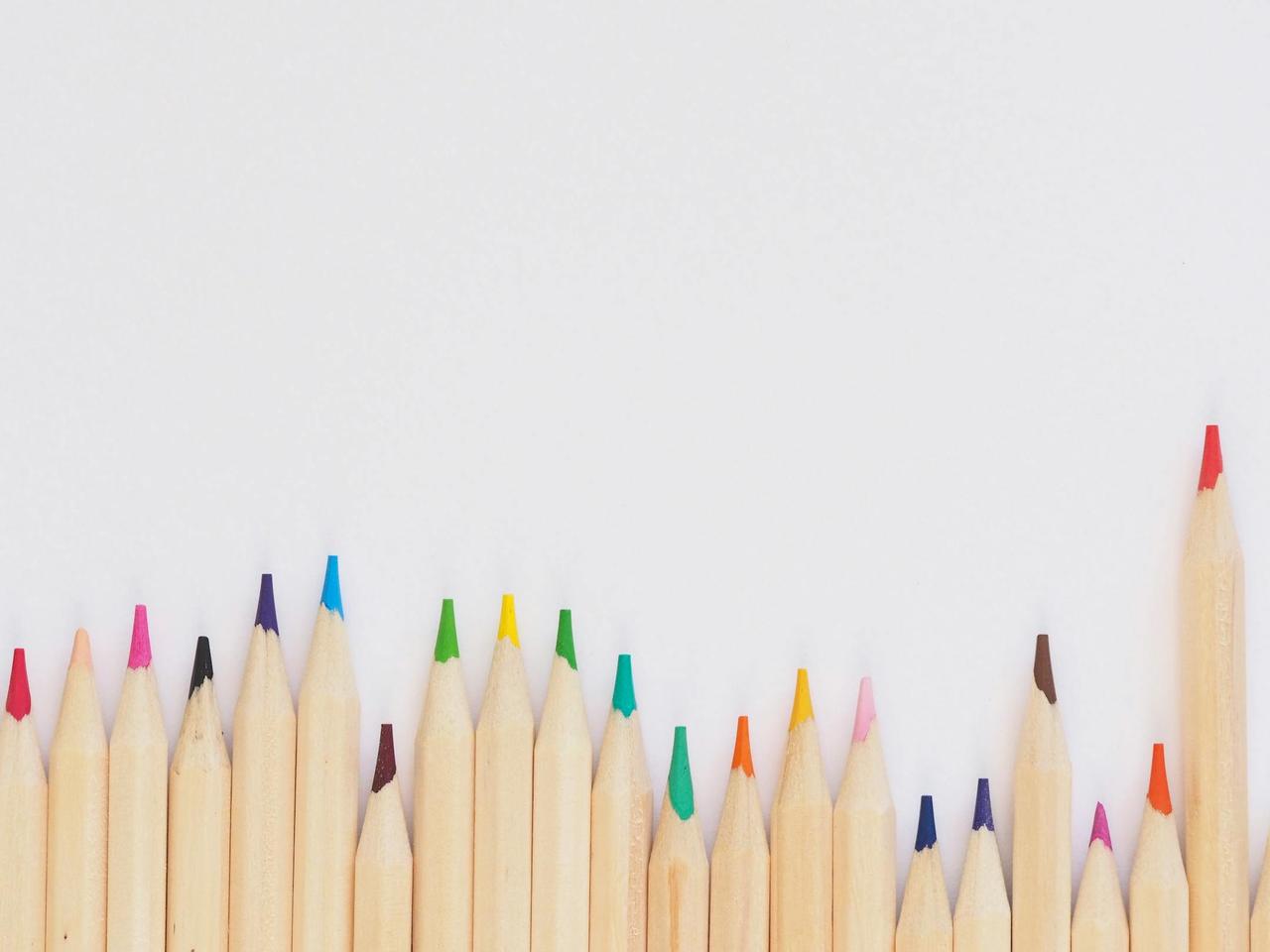 A row of vibrant colored pencils aligned on a white background, providing ample copyspace.