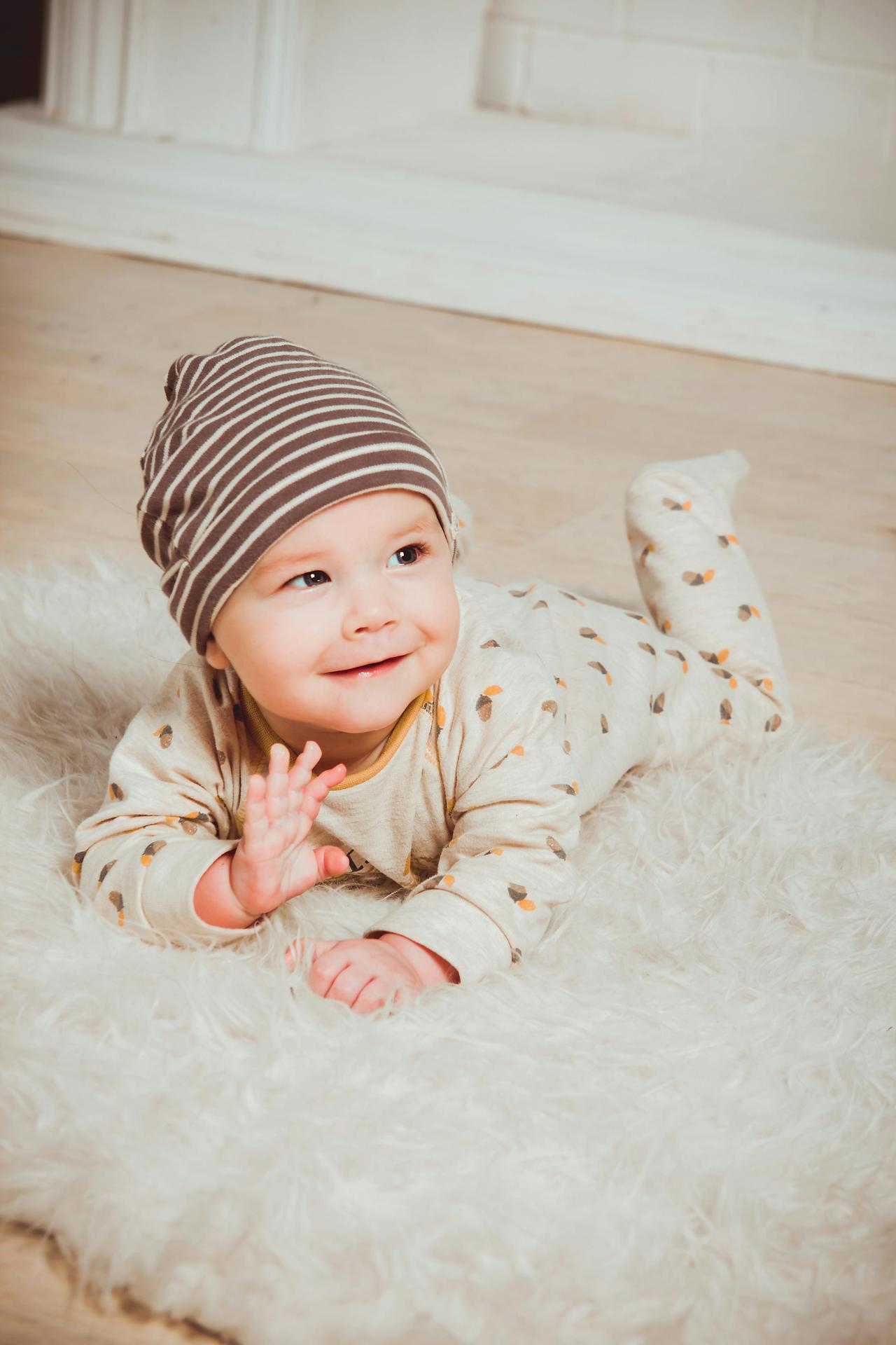 A cute baby in striped beanie lying on fluffy rug indoors, smiling with innocence.
