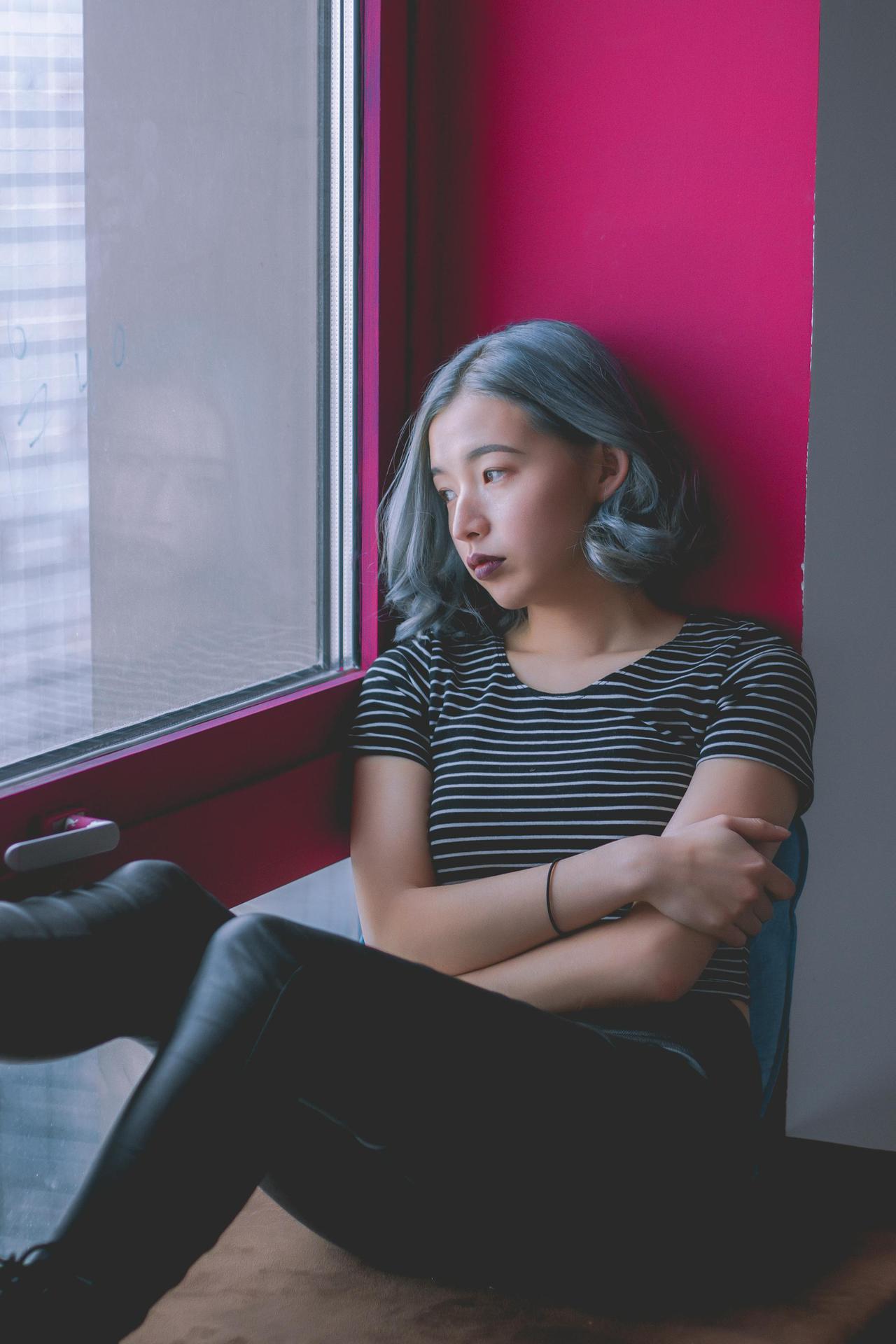 A woman sits by a window, deep in thought, conveying solitude.