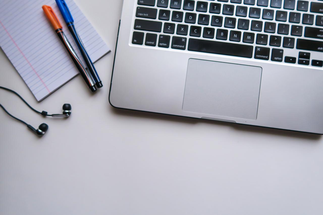 A computer with a notepad, two pens, and a pair of earbuds.
