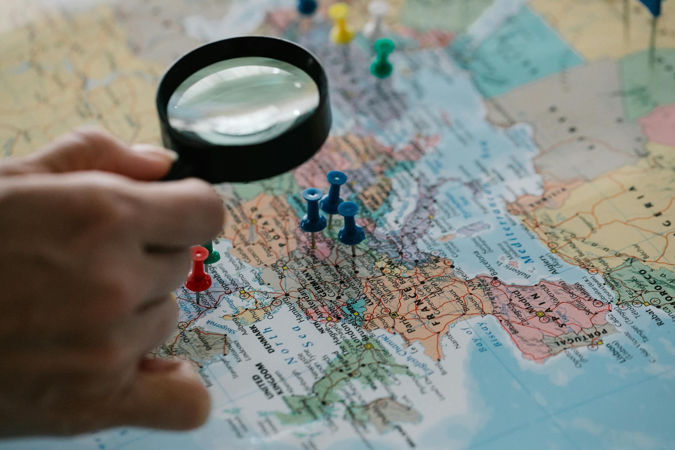 Magnifying glass focuses on pins highlighting travel destinations on a world map.