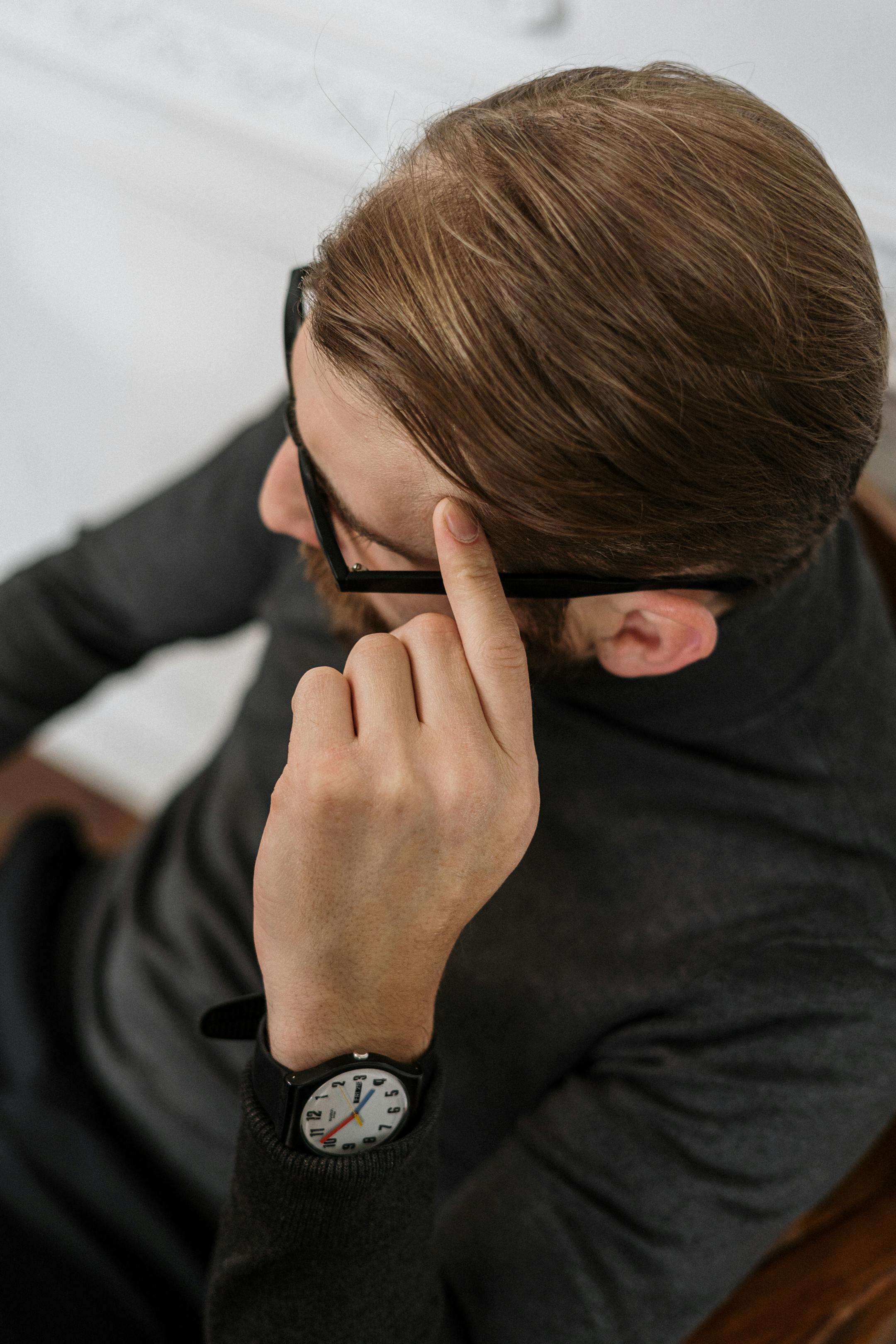 Overhead shot of a man in black turtleneck, reflecting with glasses, in a modern office setting.