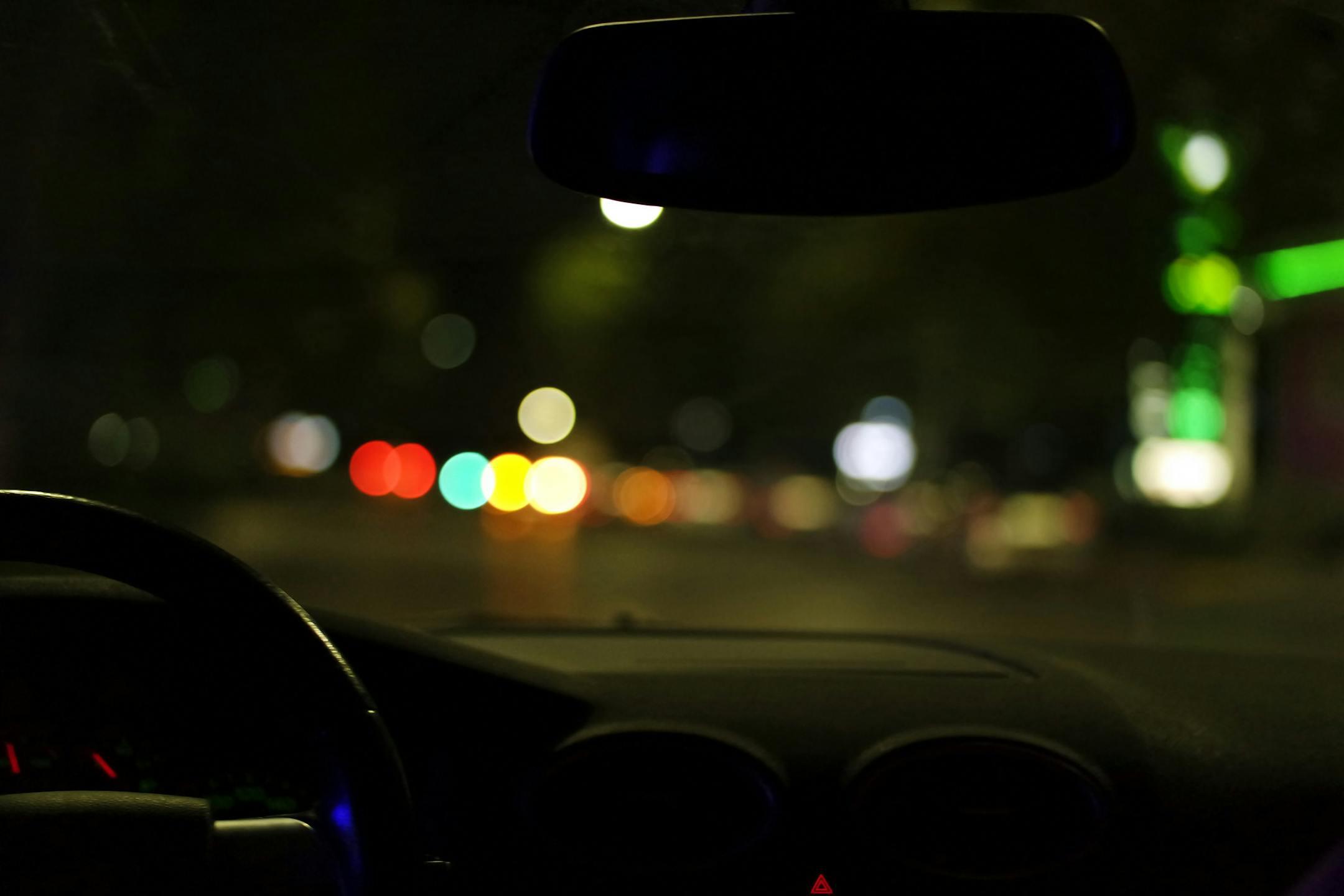 Blurred city lights seen from a car interior at night, depicting urban driving ambiance.