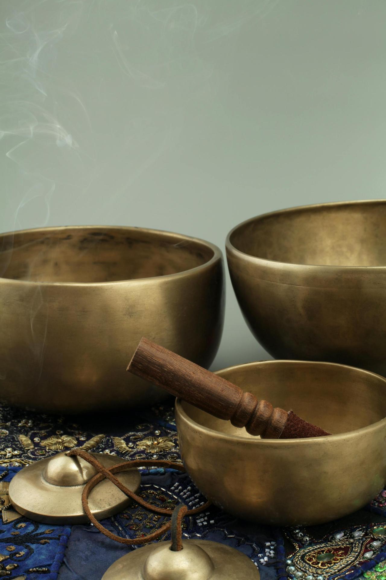 Close-up of antique bronze singing bowls with a wooden stick and smoke on a decorative cloth.