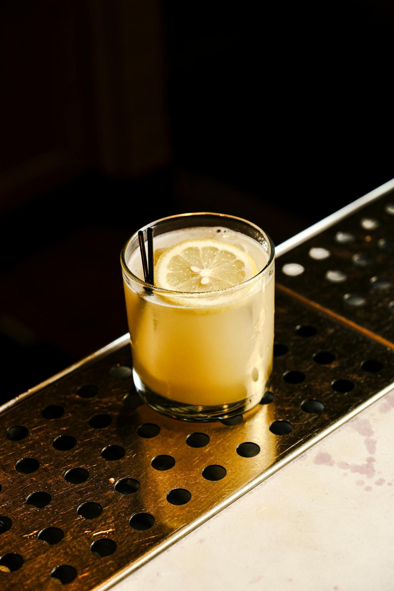 A citrus cocktail garnished with a lemon slice on a stylish metal bar counter.