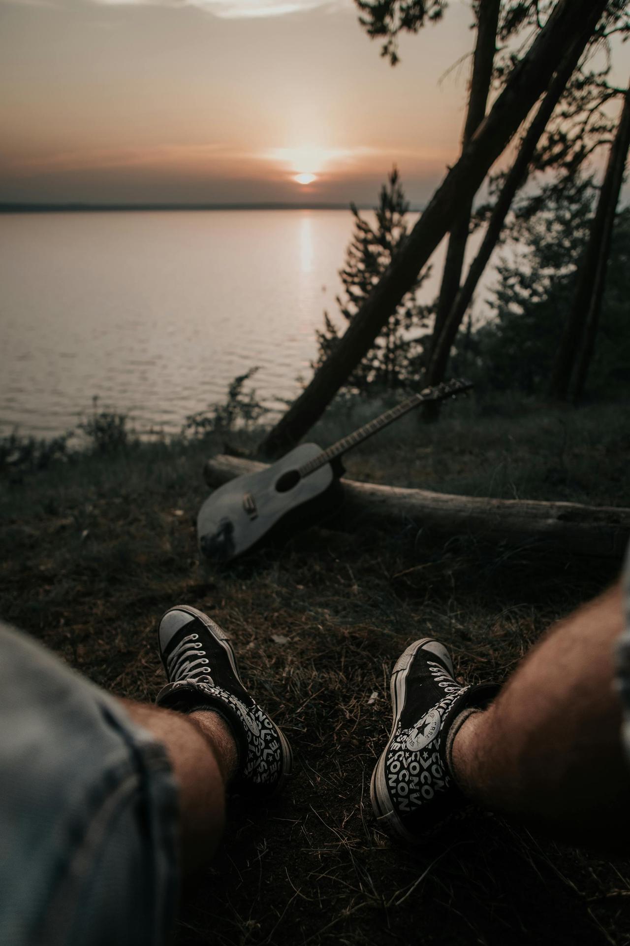 Relaxing by the lake at sunset with an acoustic guitar, capturing serenity and nature's beauty.