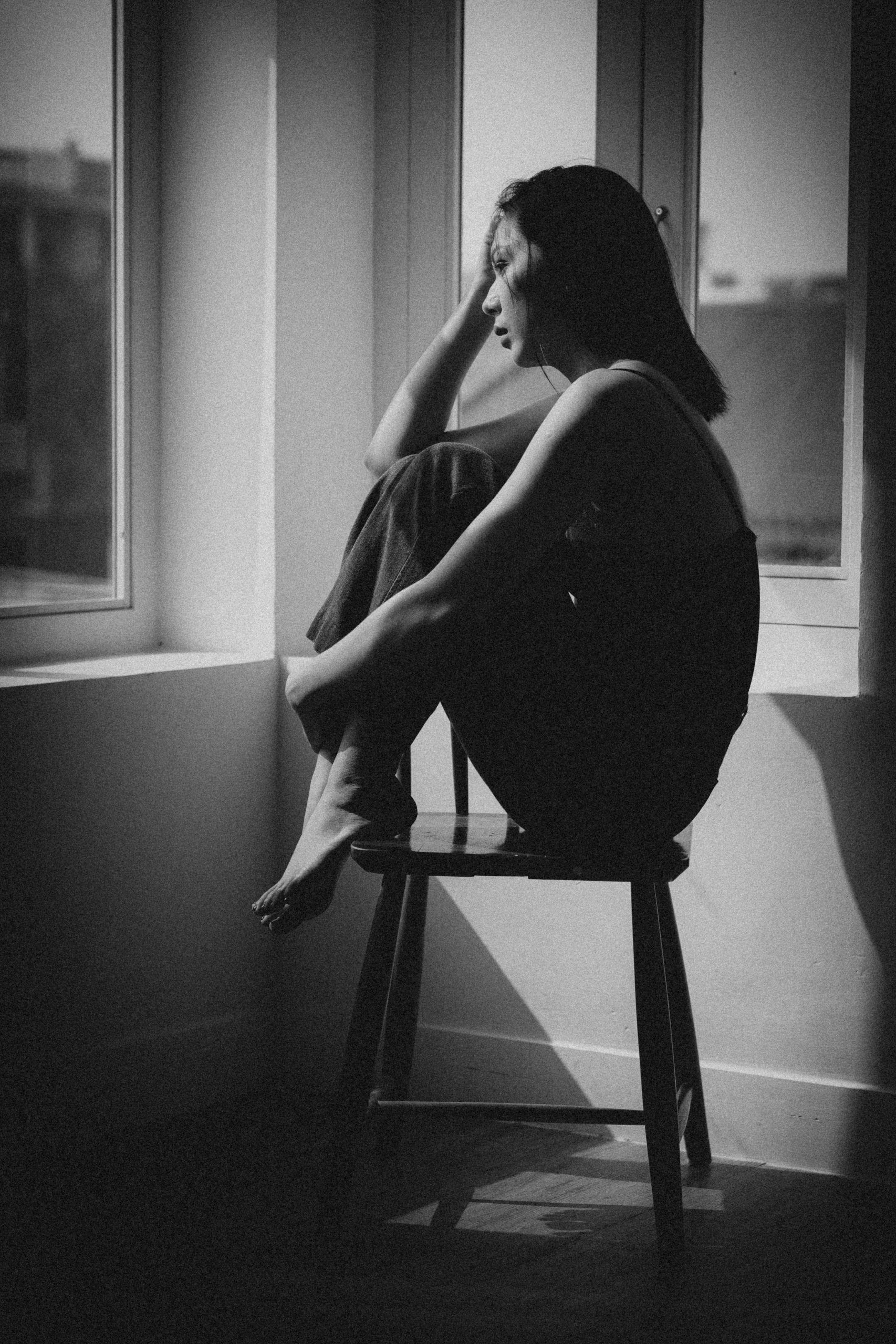A woman sitting on a chair by a window, deep in thought, creating a serene mood.