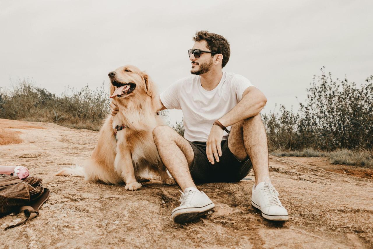 A man sitting outdoors with a Golden Retriever, enjoying a relaxing moment.
