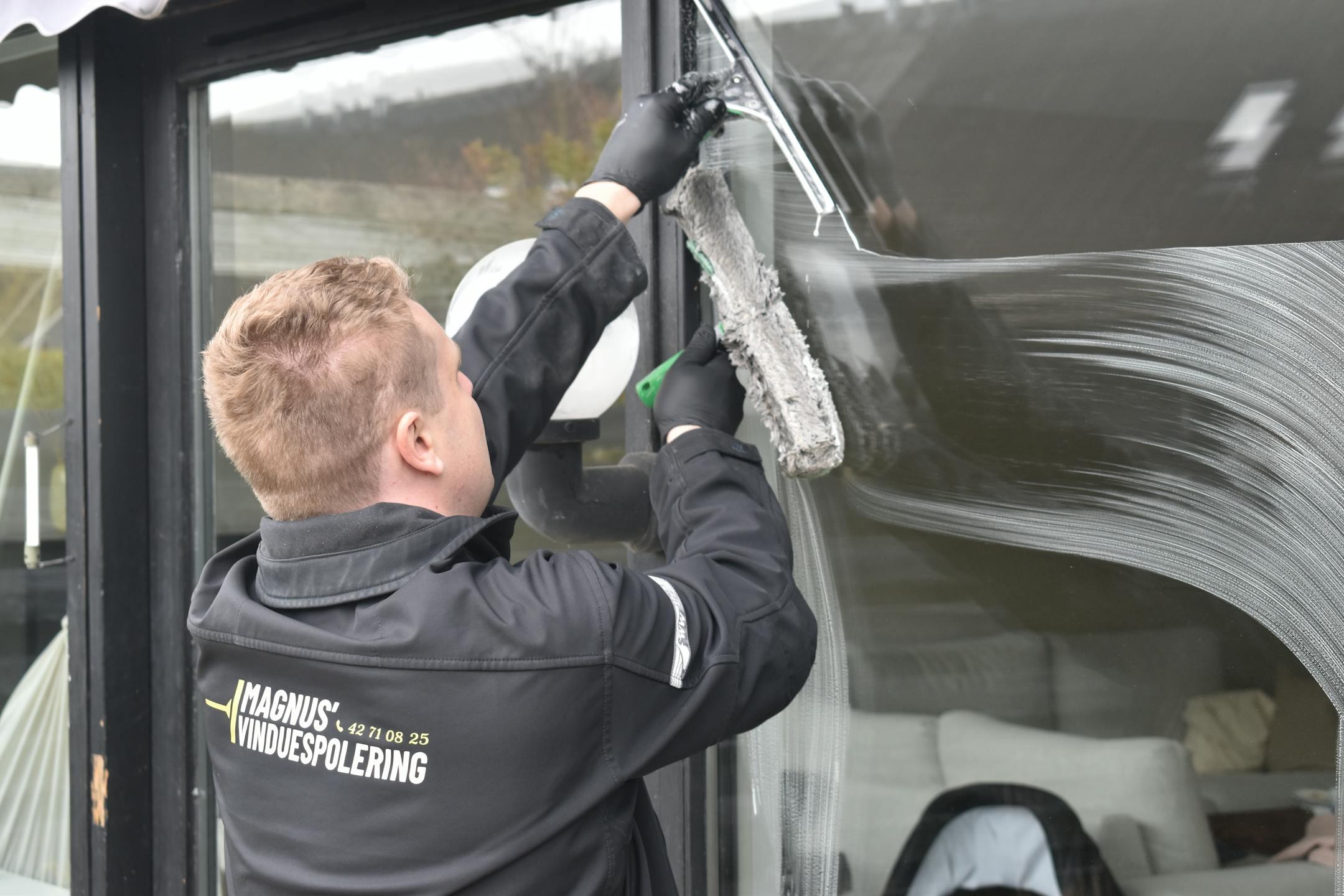 <strong>Professional window cleaner cleaning a large residential window with a squeegee</strong>