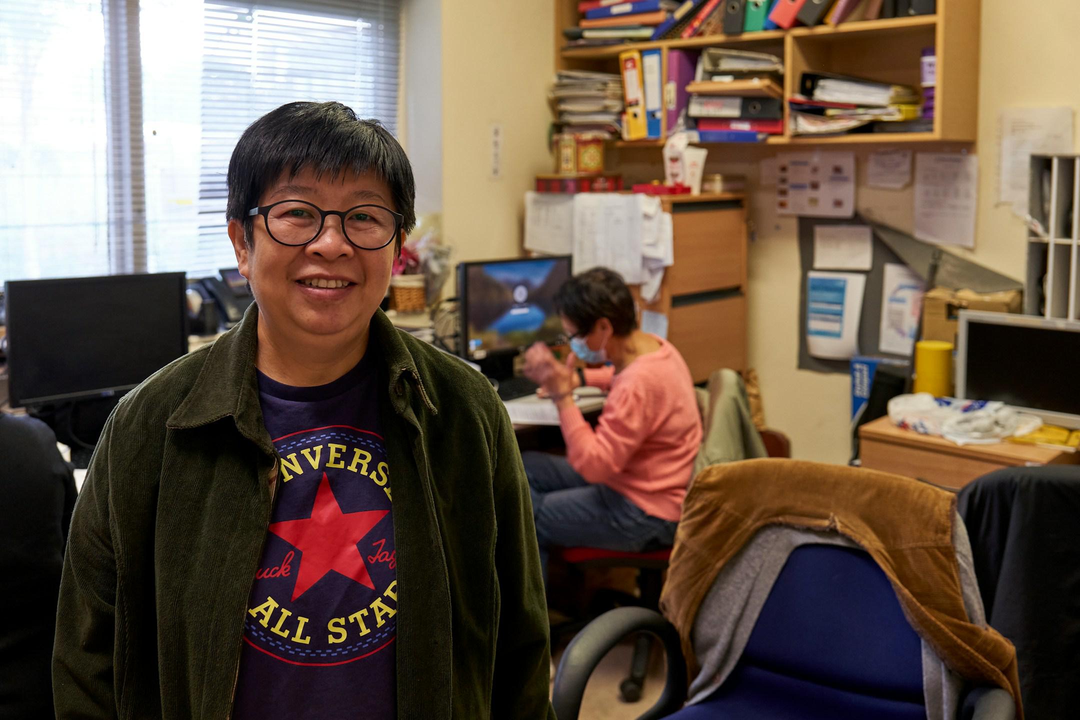 Woman standing in an office. She's standing and smiling at the camera.