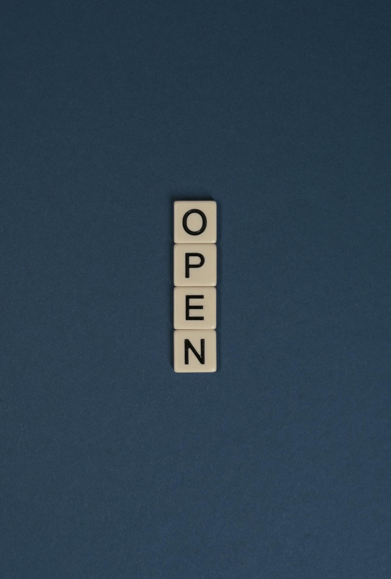 Scrabble tiles spelling 'OPEN' vertically on a blue background, ideal for copyspace.