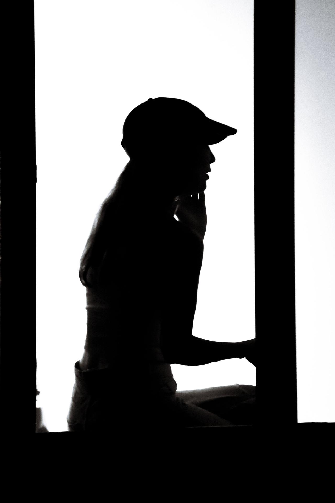 Silhouette of a woman sitting by a window in contemplation. Artistic portrayal with strong contrast.
