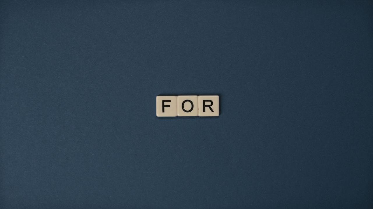 Artistic display of Scrabble tiles spelling the word 'For' on a dark background.