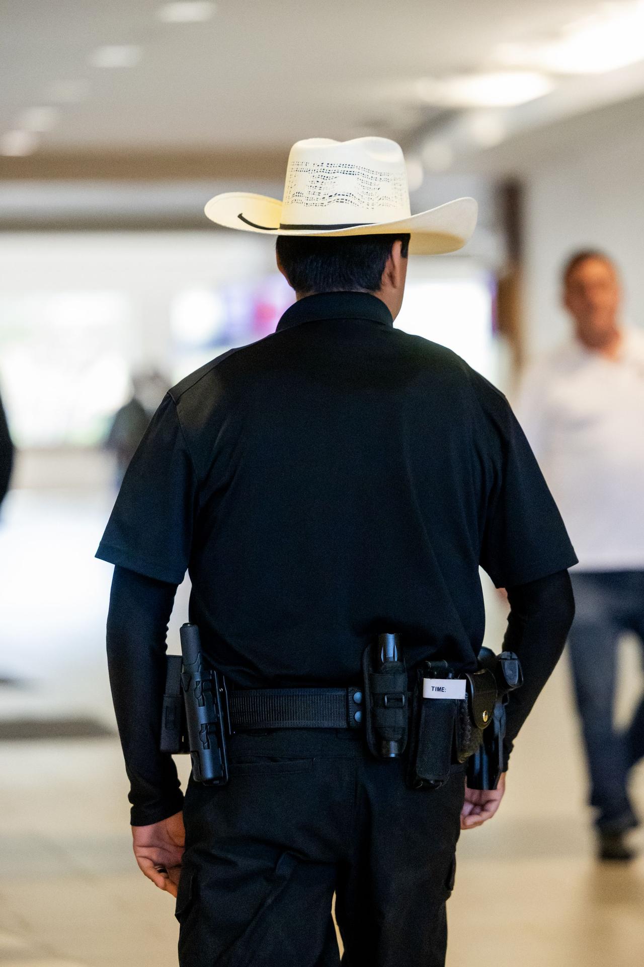 Security guard with cowboy hat patrolling inside a building, showcasing law enforcement and security themes.