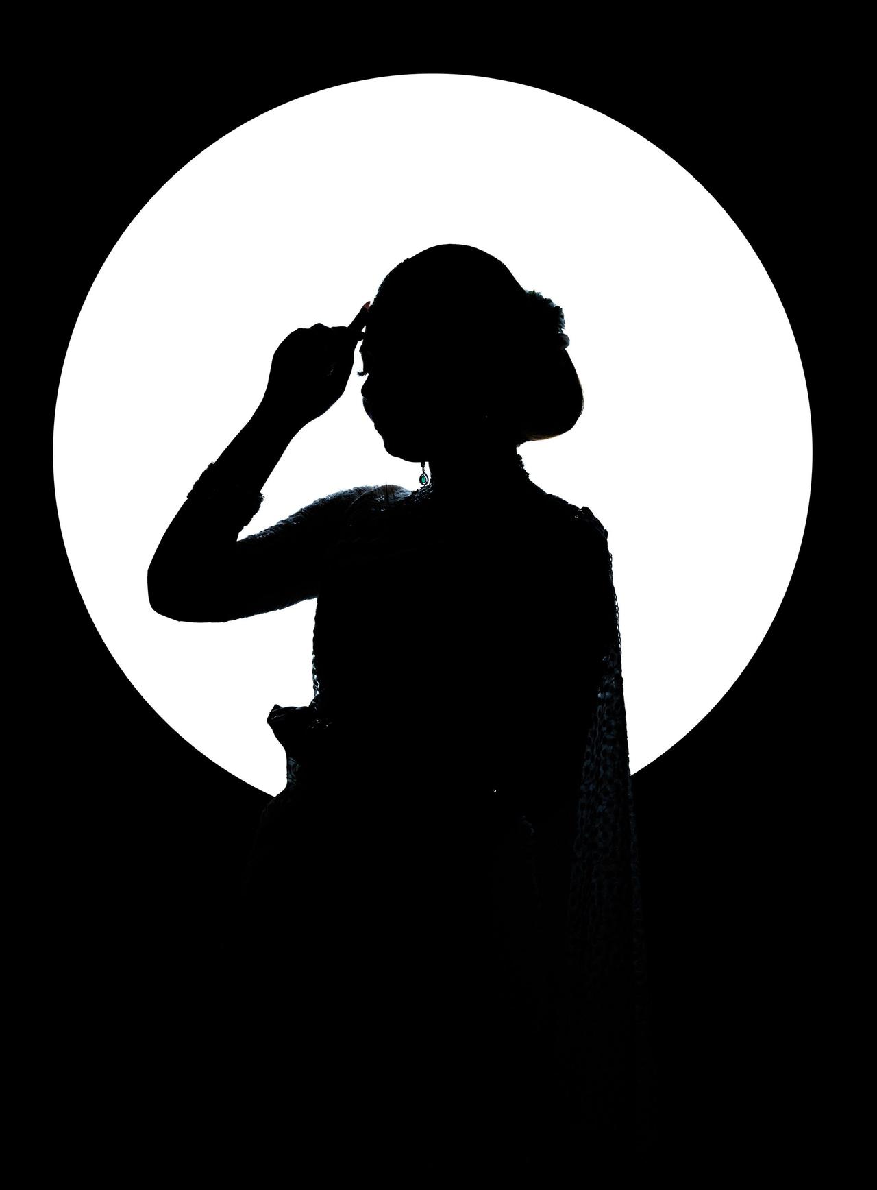 Silhouetted figure in artistic pose against a bright moon-like backdrop.