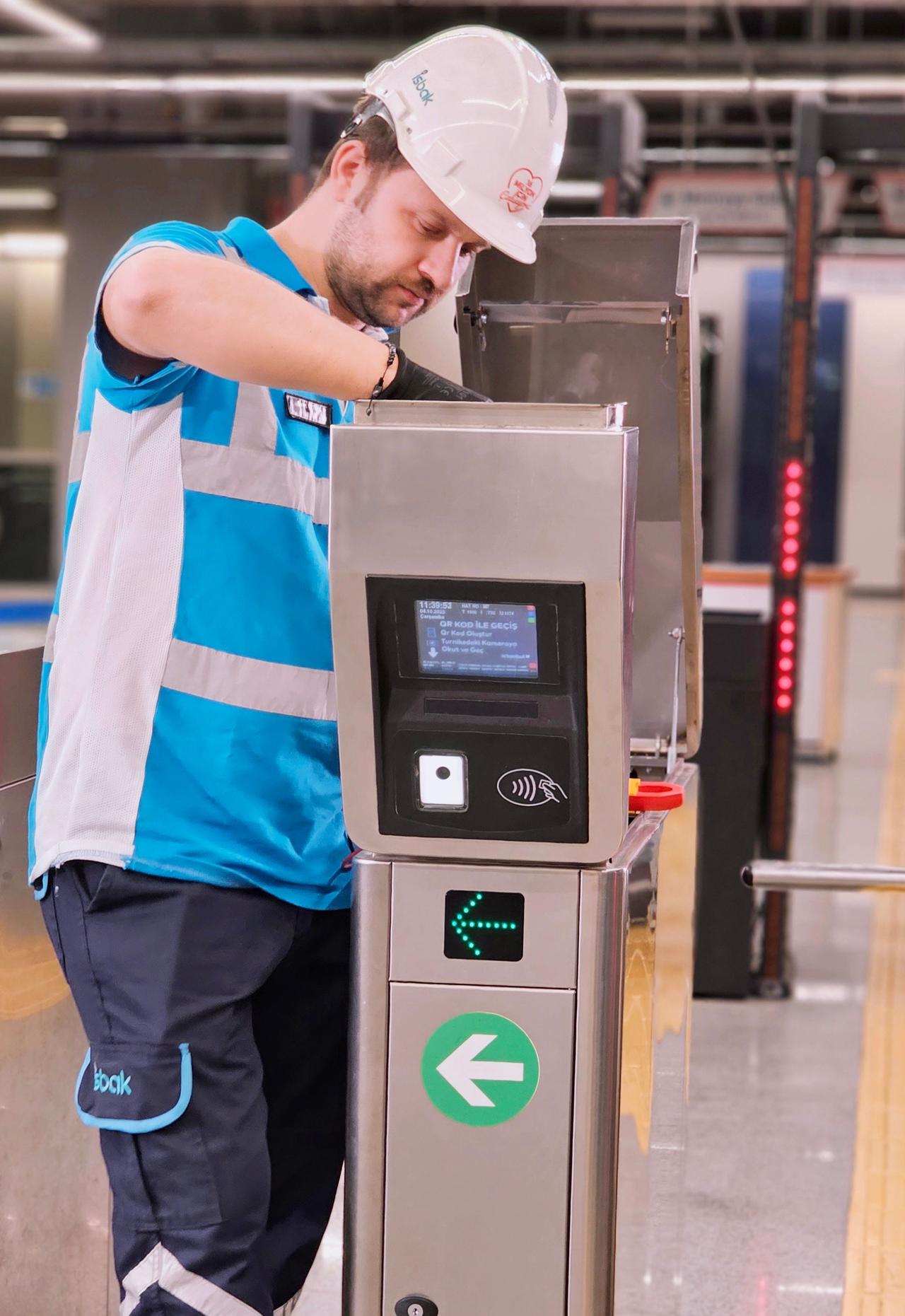 A worker in a helmet repairs a metro station turnstile gate, ensuring public transportation efficiency.
