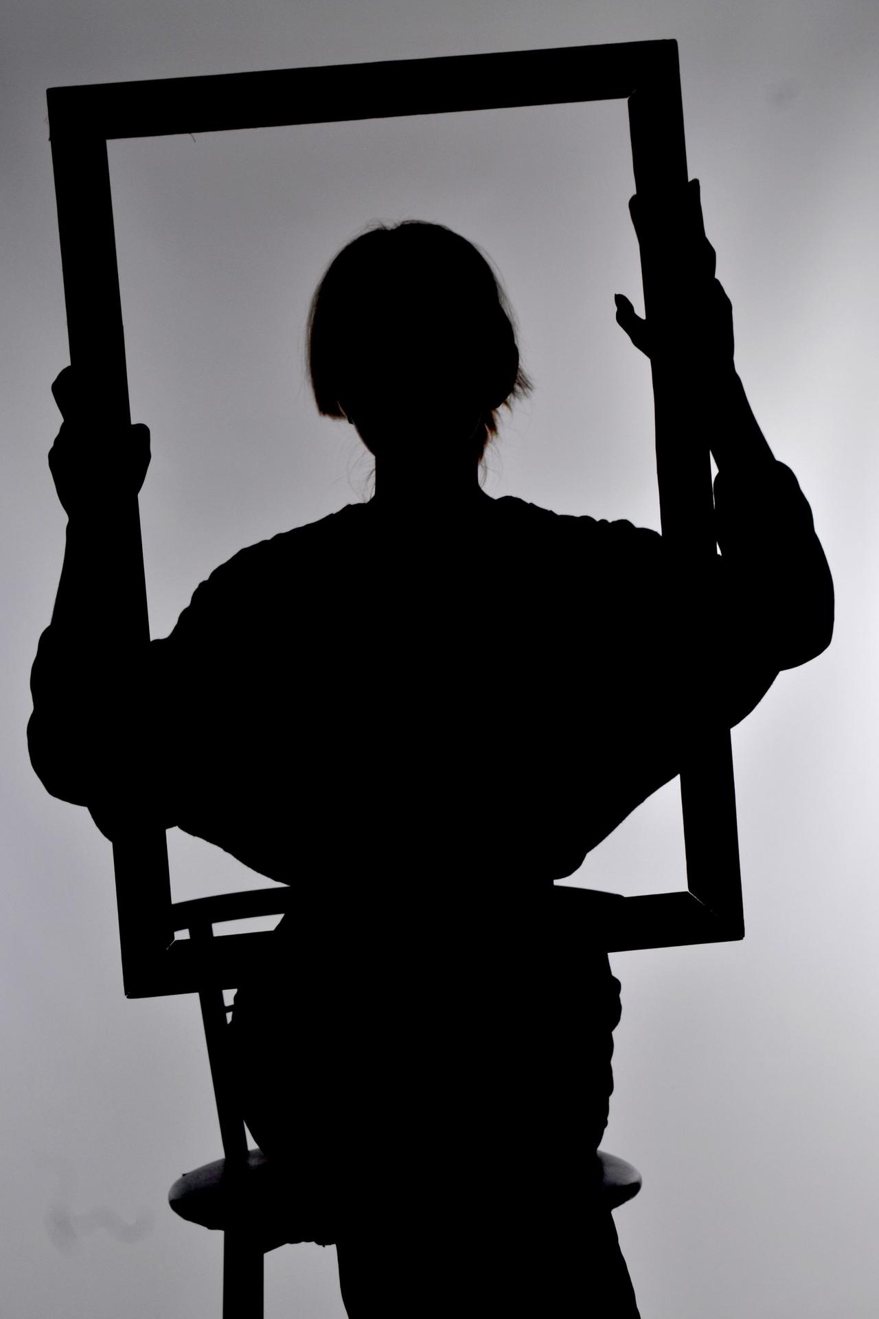 Artistic silhouette of a woman sitting and holding a frame in a studio setting.