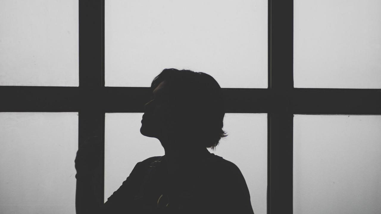 A striking silhouette of a person posing against large window panels.