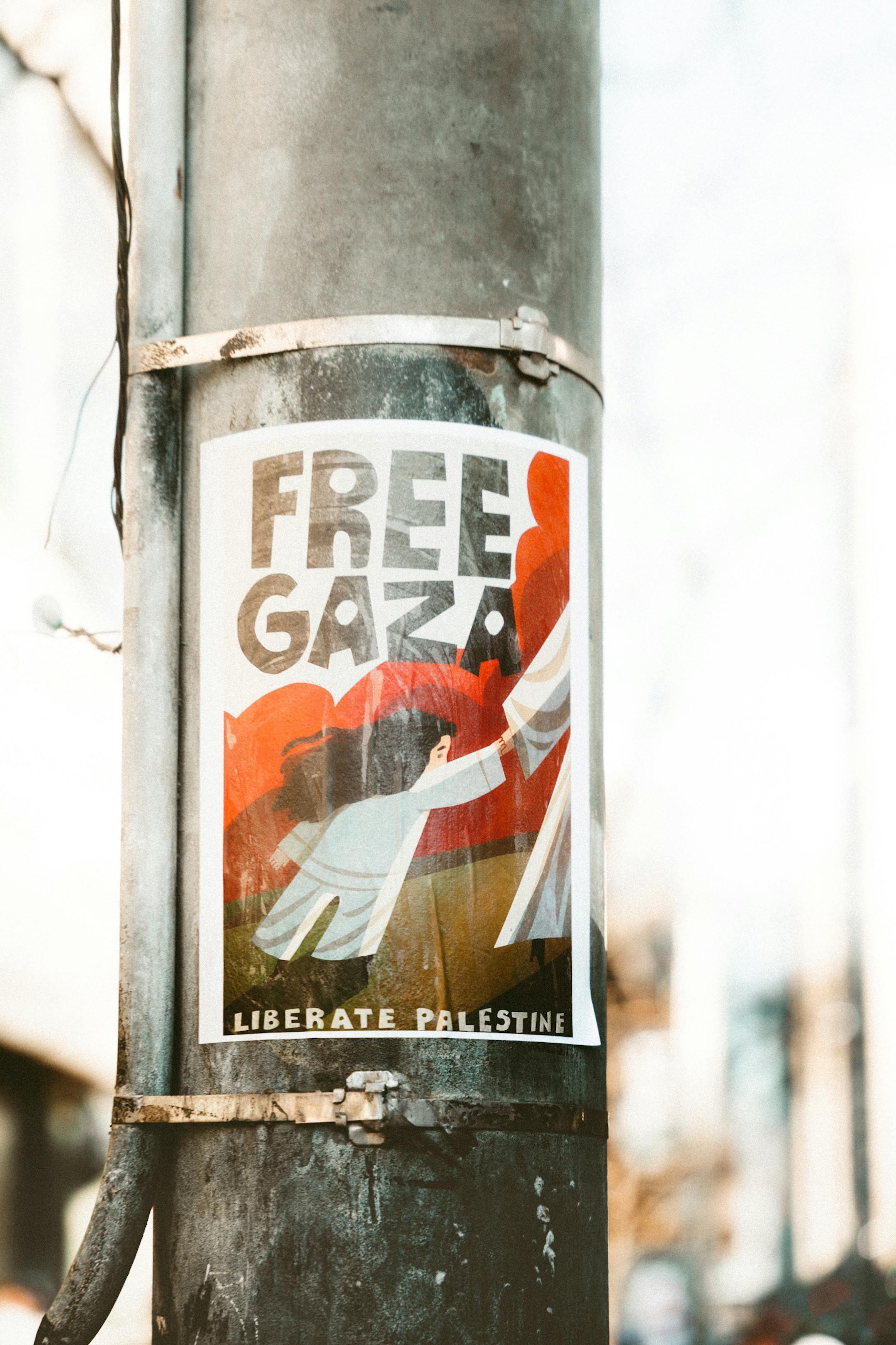 A poster advocating for Gaza freedom attached to a street lamp in an urban setting.