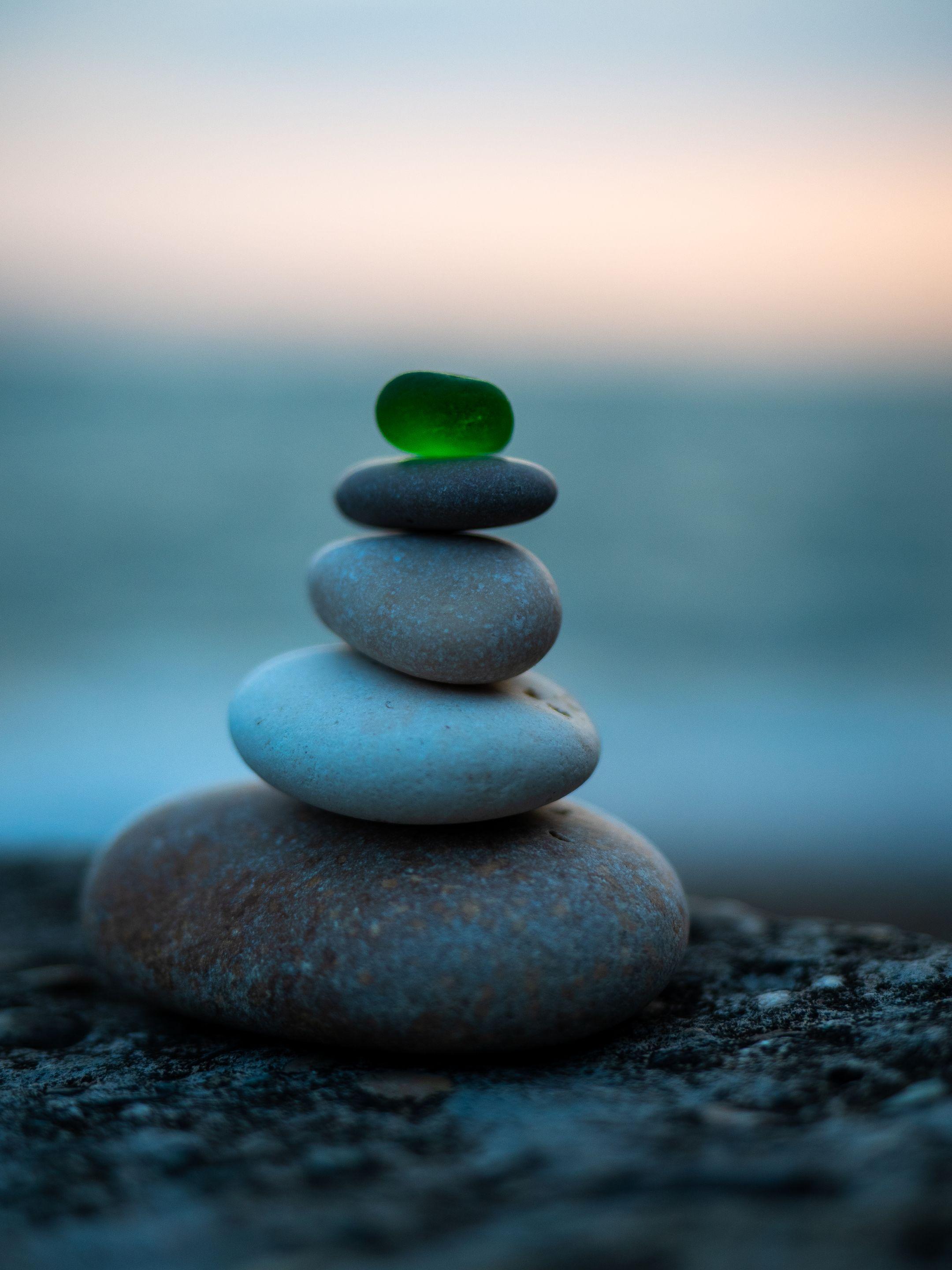 A creative stack of stones topped with sea glass on a beach with a blurred ocean background.