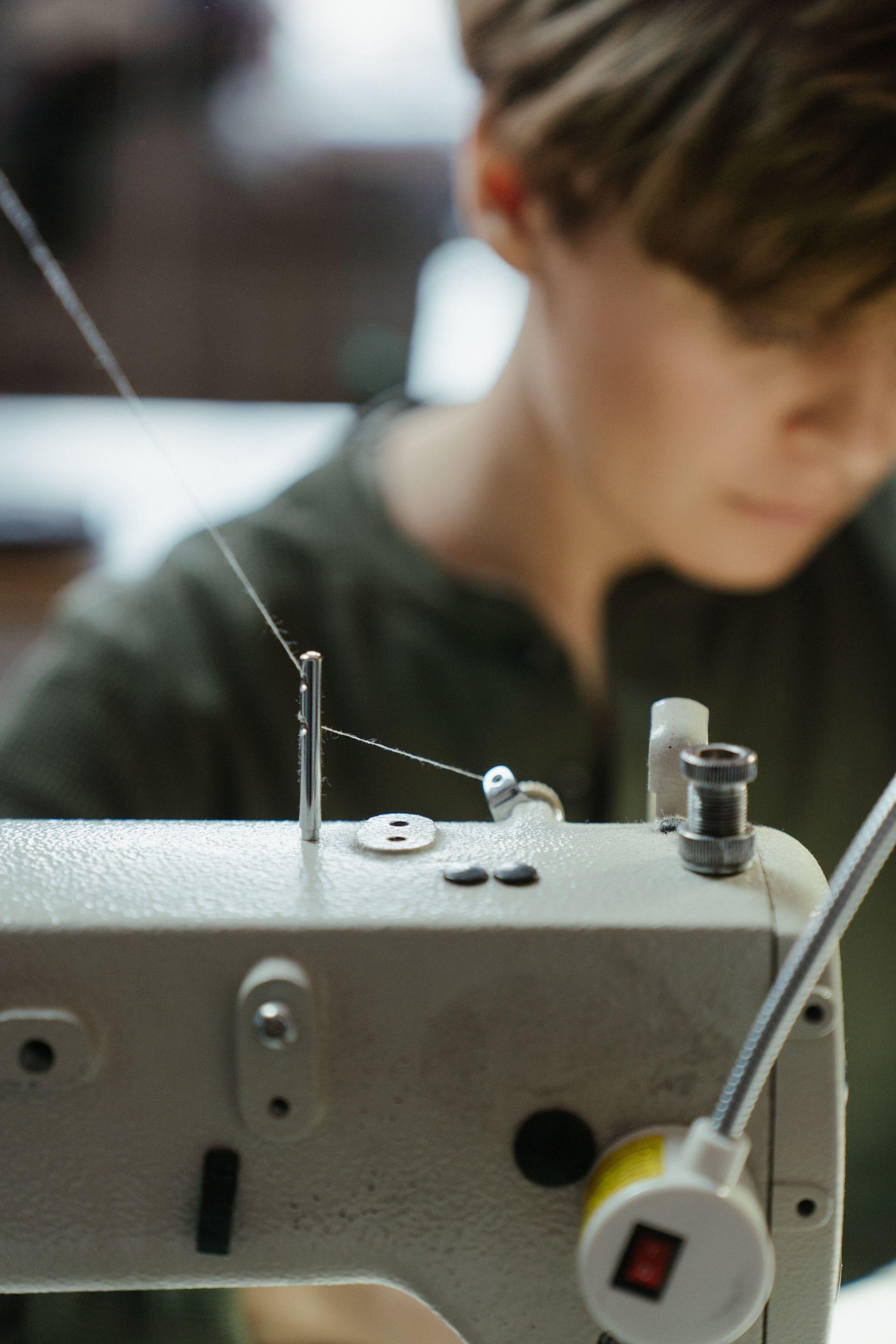 Tailor using a sewing machine in a workshop setting, focused on needlework.