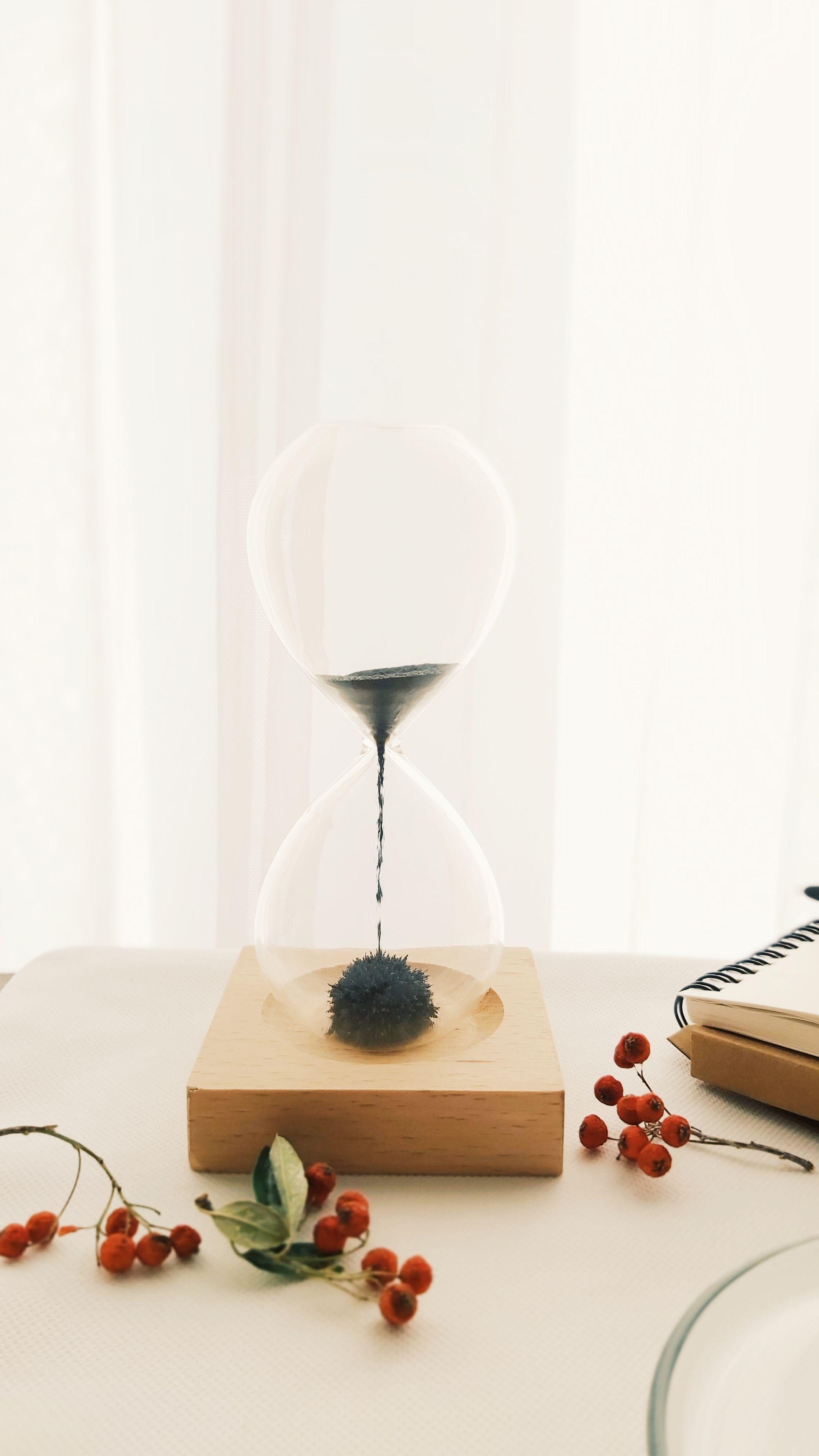 Stylish hourglass on a wooden base adorned with red berries on a table, showcasing timeless elegance.
