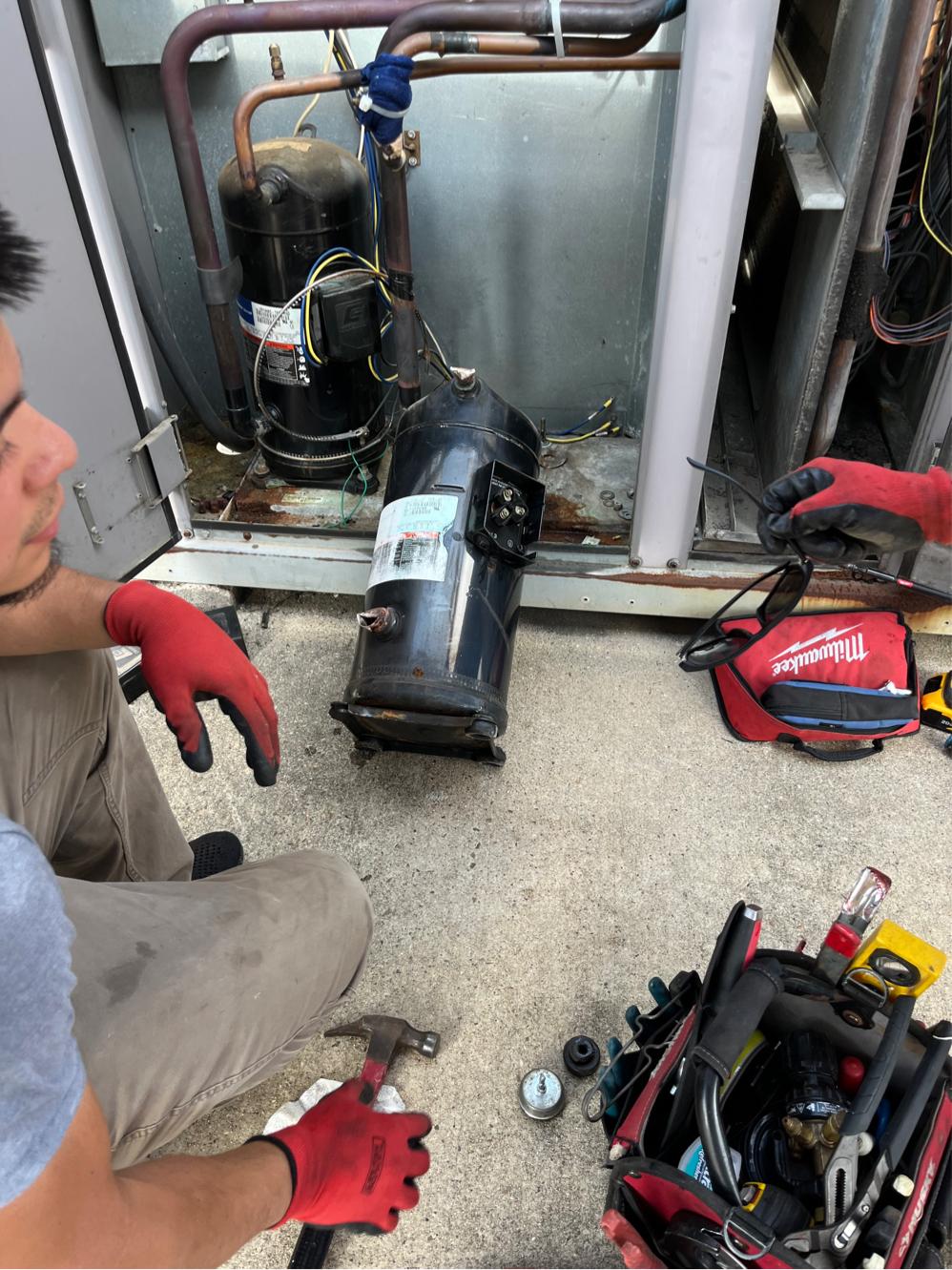 Technician removing the failed AC compressor from the condenser