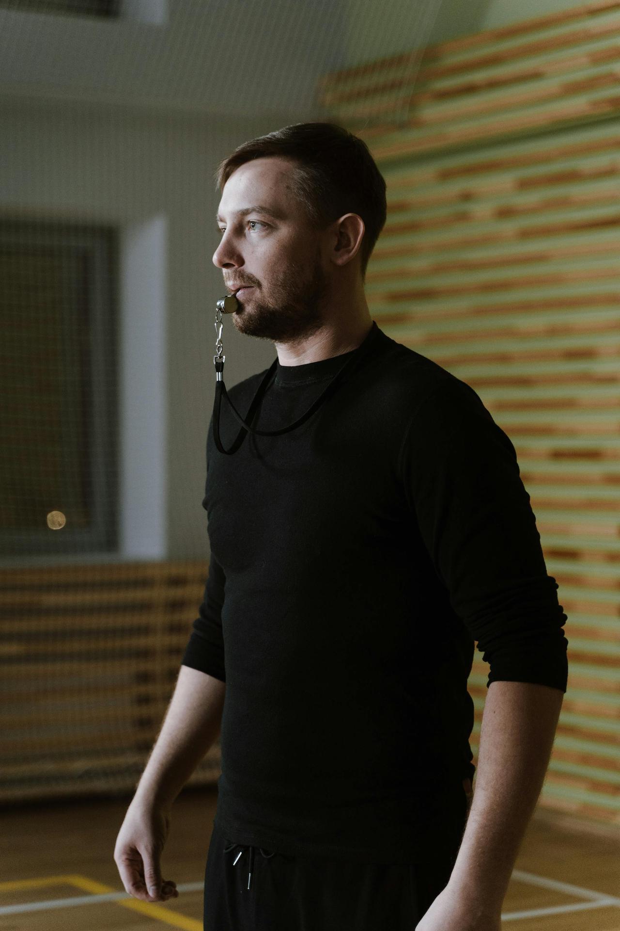 Portrait of a sports coach wearing black long sleeves indoors with a whistle.