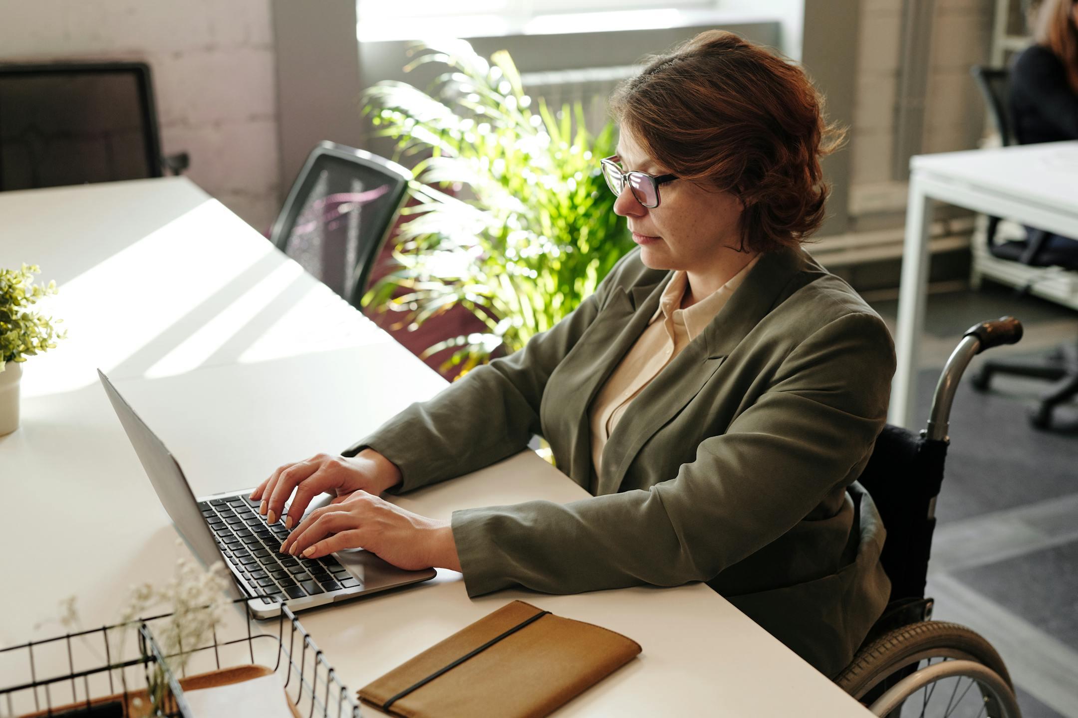 Businesswoman in wheelchair using laptop at office desk.
