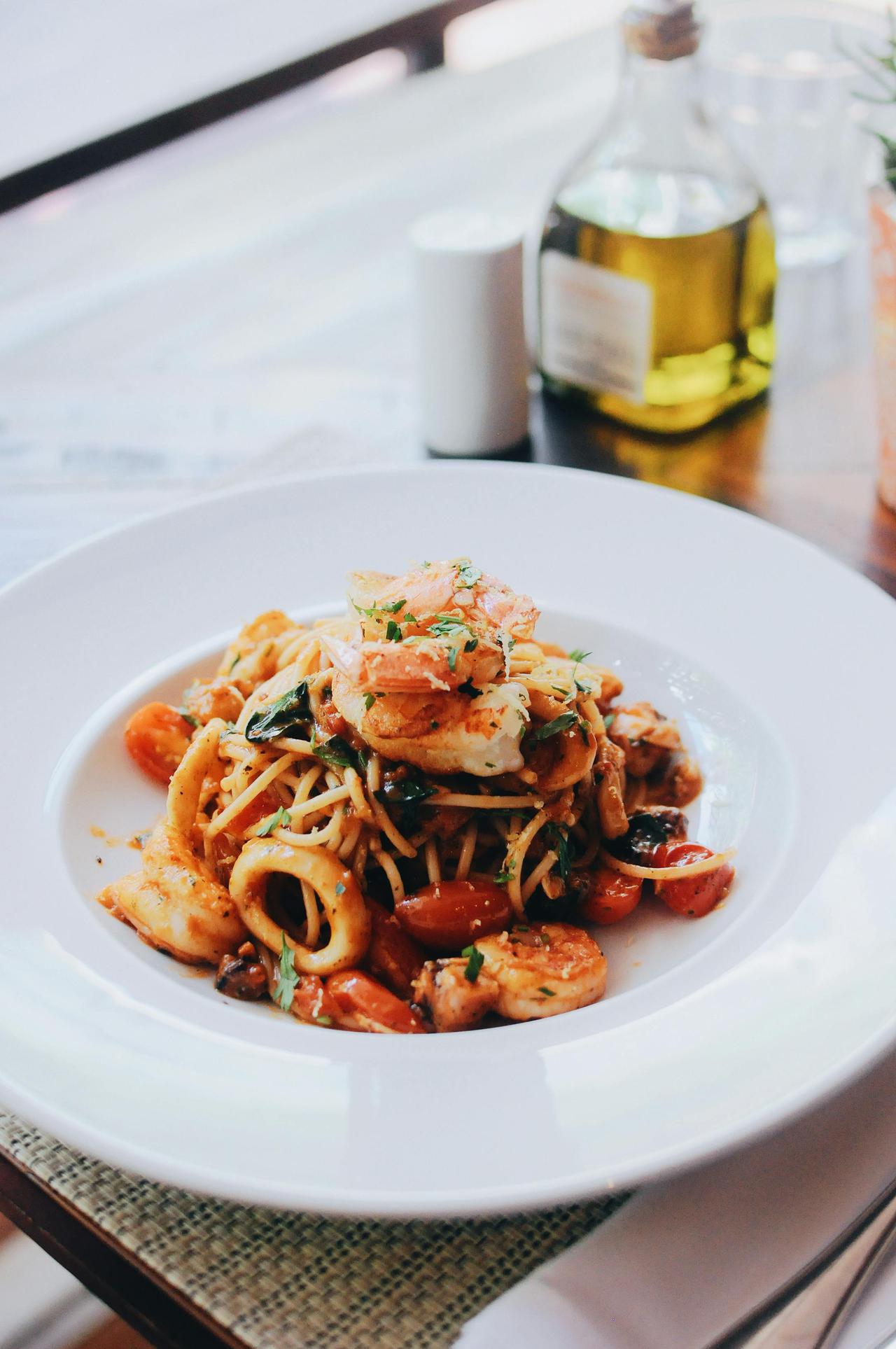 Plate of spaghetti with shrimp and calamari garnished with herbs, captured indoors.