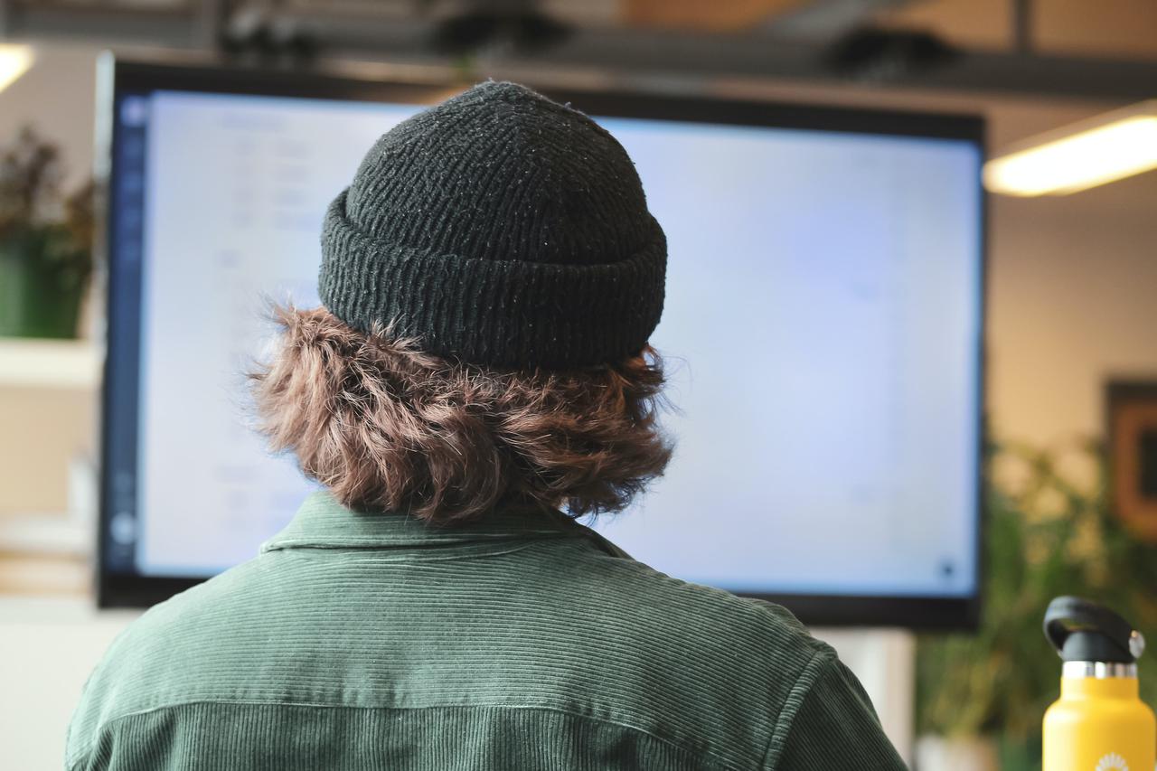 An employee in a beanie and geen shirt using a computer. The best business IT solutions account for gaps made by human error.