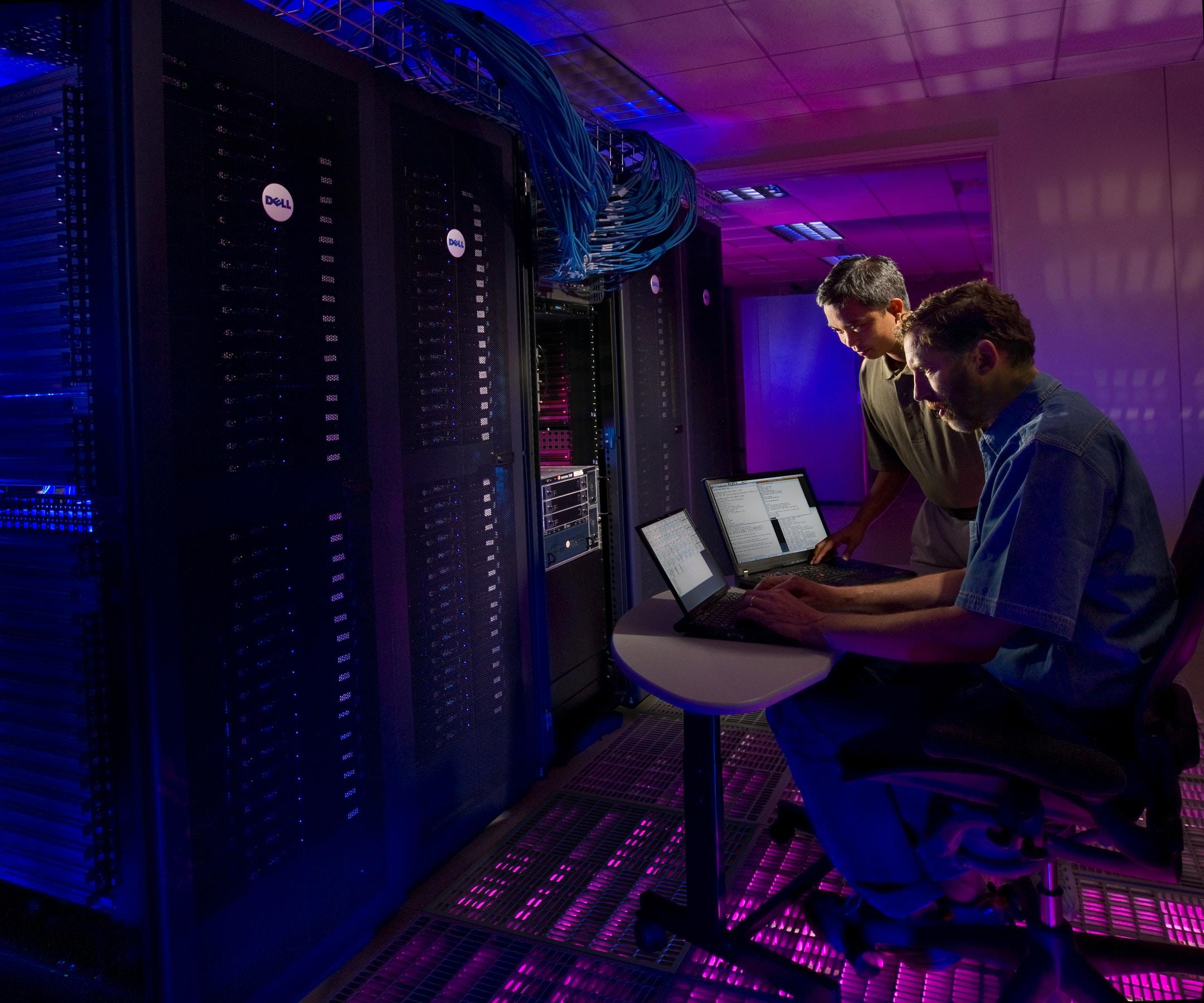 Image of two Medford computer specialists working on a server in a room lit with purple light.