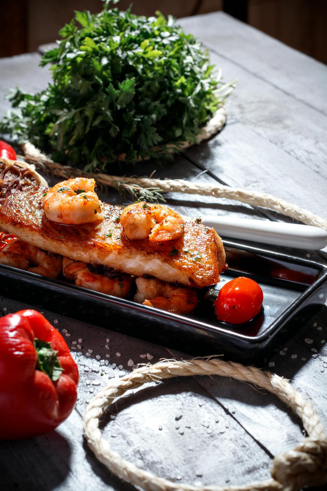 A mouthwatering dish of grilled fish topped with shrimp, garnished with vegetables.