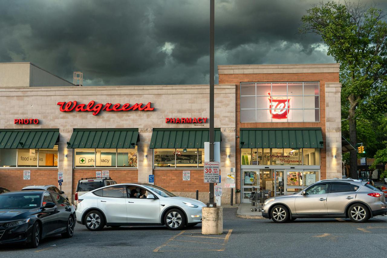Exterior view of a Walgreens pharmacy under dark storm clouds with cars in the parking lot.