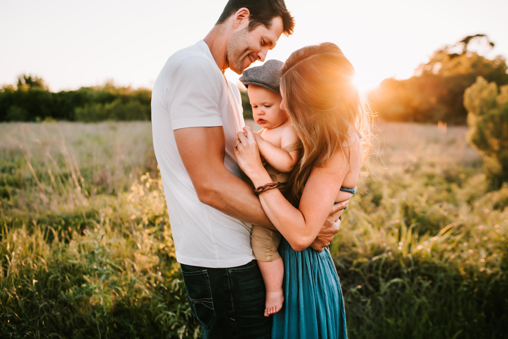 man and woman hlding baby in field at sunset