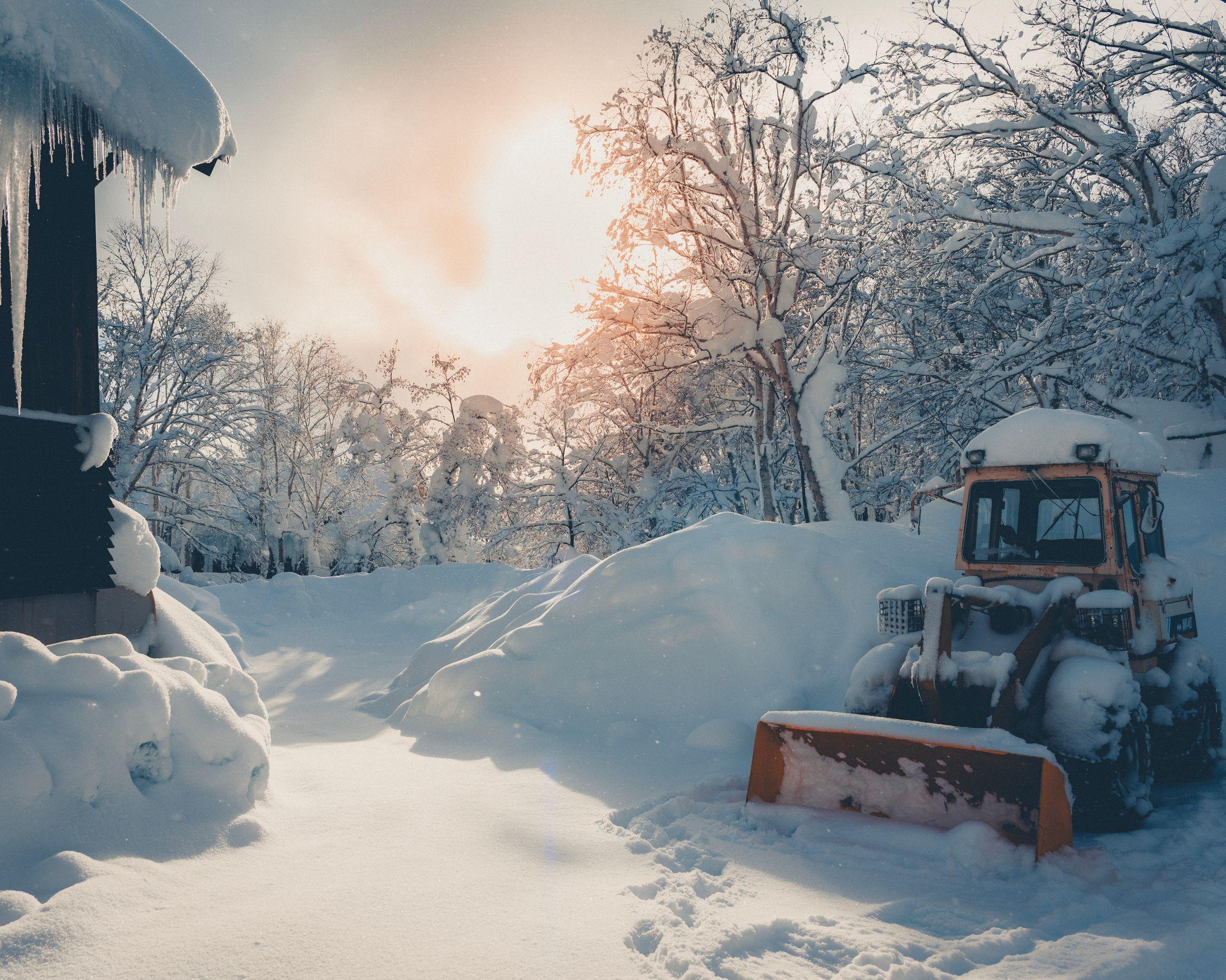 A serene winter scene showing a snow-covered tractor at sunrise in the countryside.