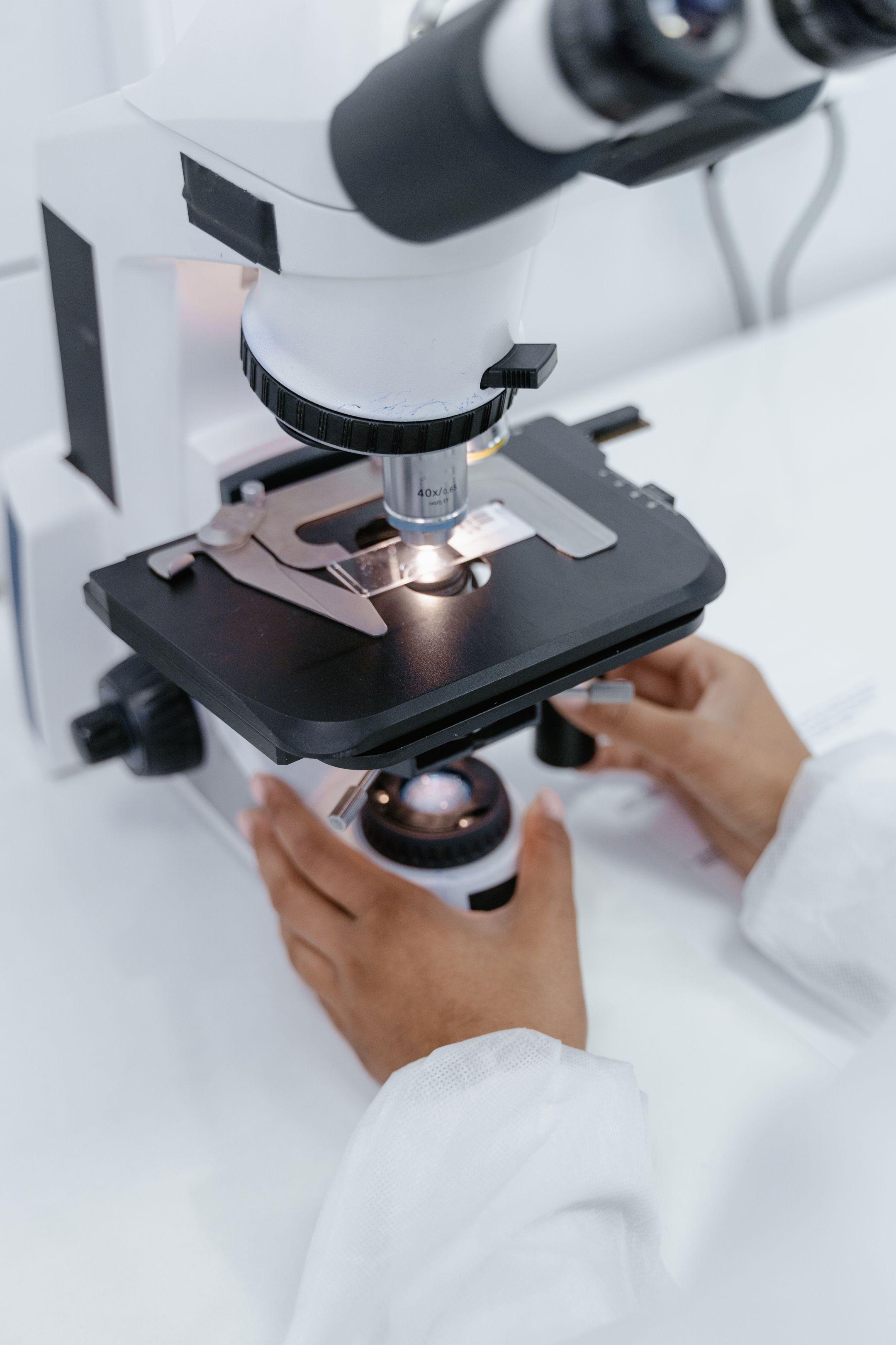 Scientist's hands operating a microscope in a laboratory setting for research purposes.