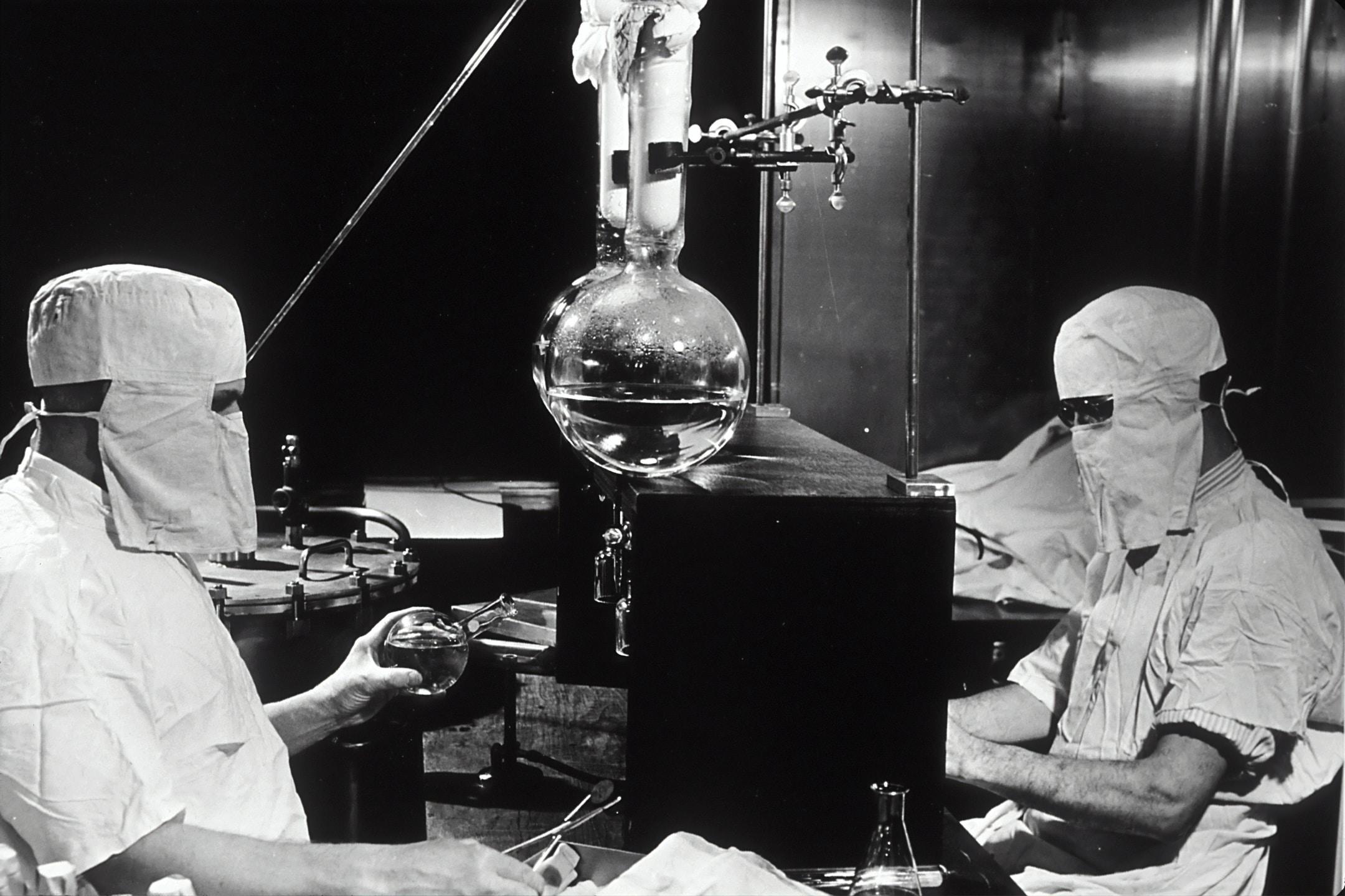Generic laboratory shot circa 1950 - researchers garbed with full mask and head covering and laboratory equipment.