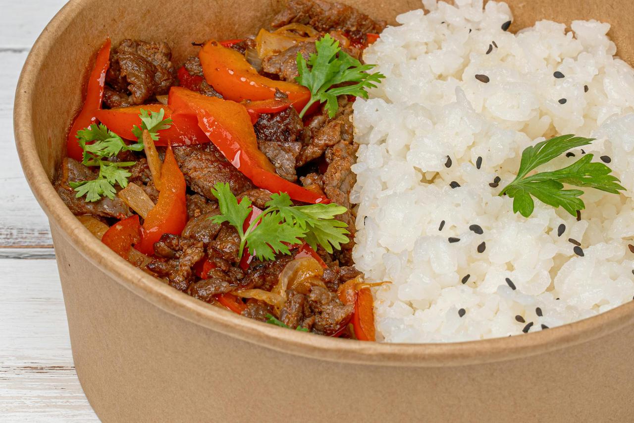 Close-up of a savory beef and vegetables dish with rice in a paper bowl.