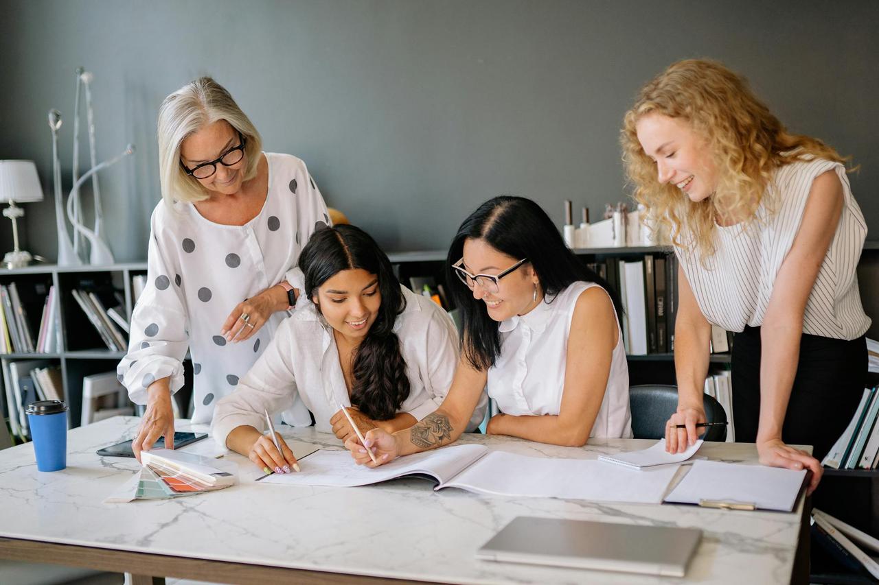 Four diverse women brainstorming ideas in a modern office environment with enthusiasm.