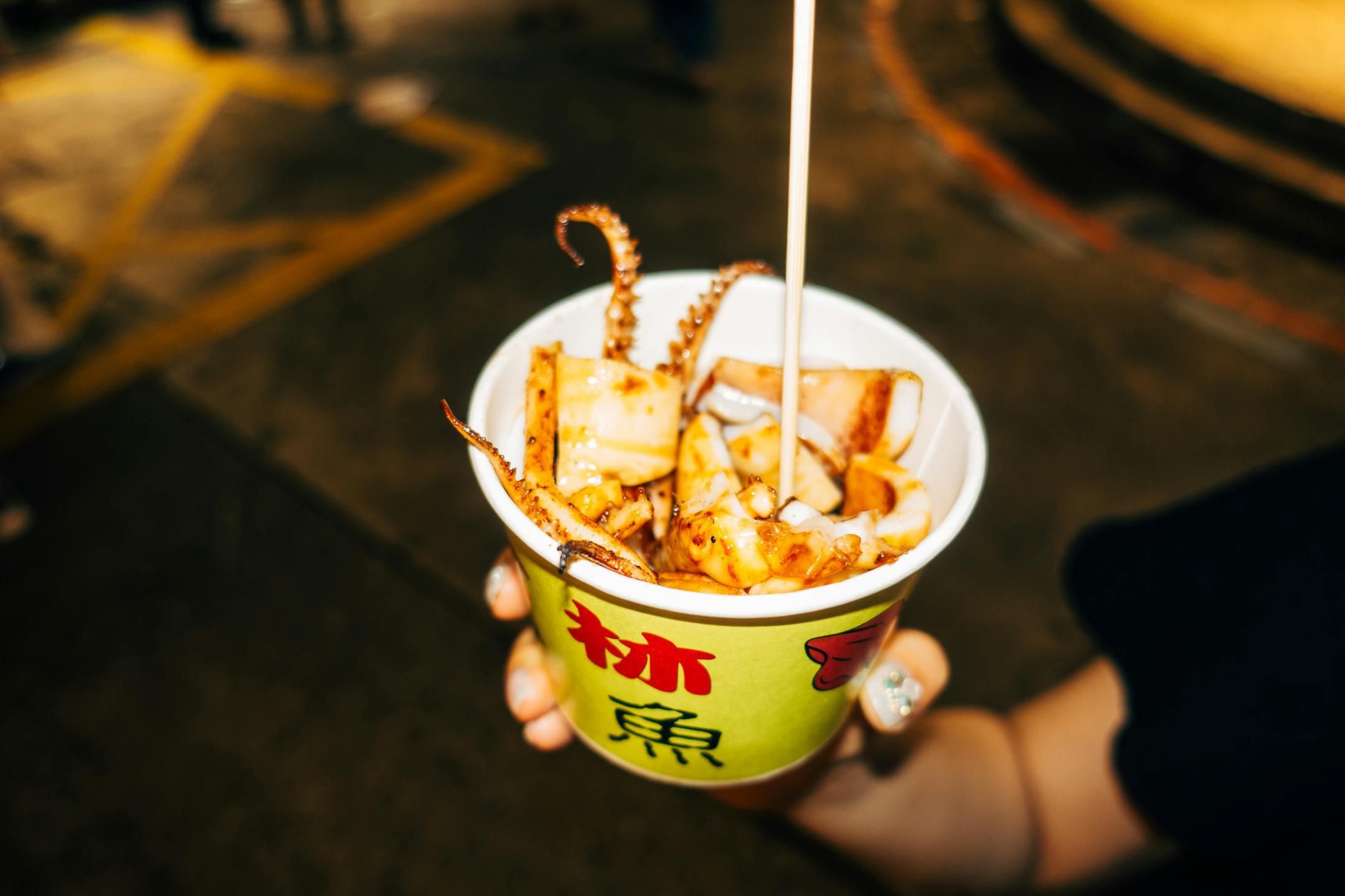 Delicious street food featuring grilled squid served in a paper cup, perfect for seafood lovers.