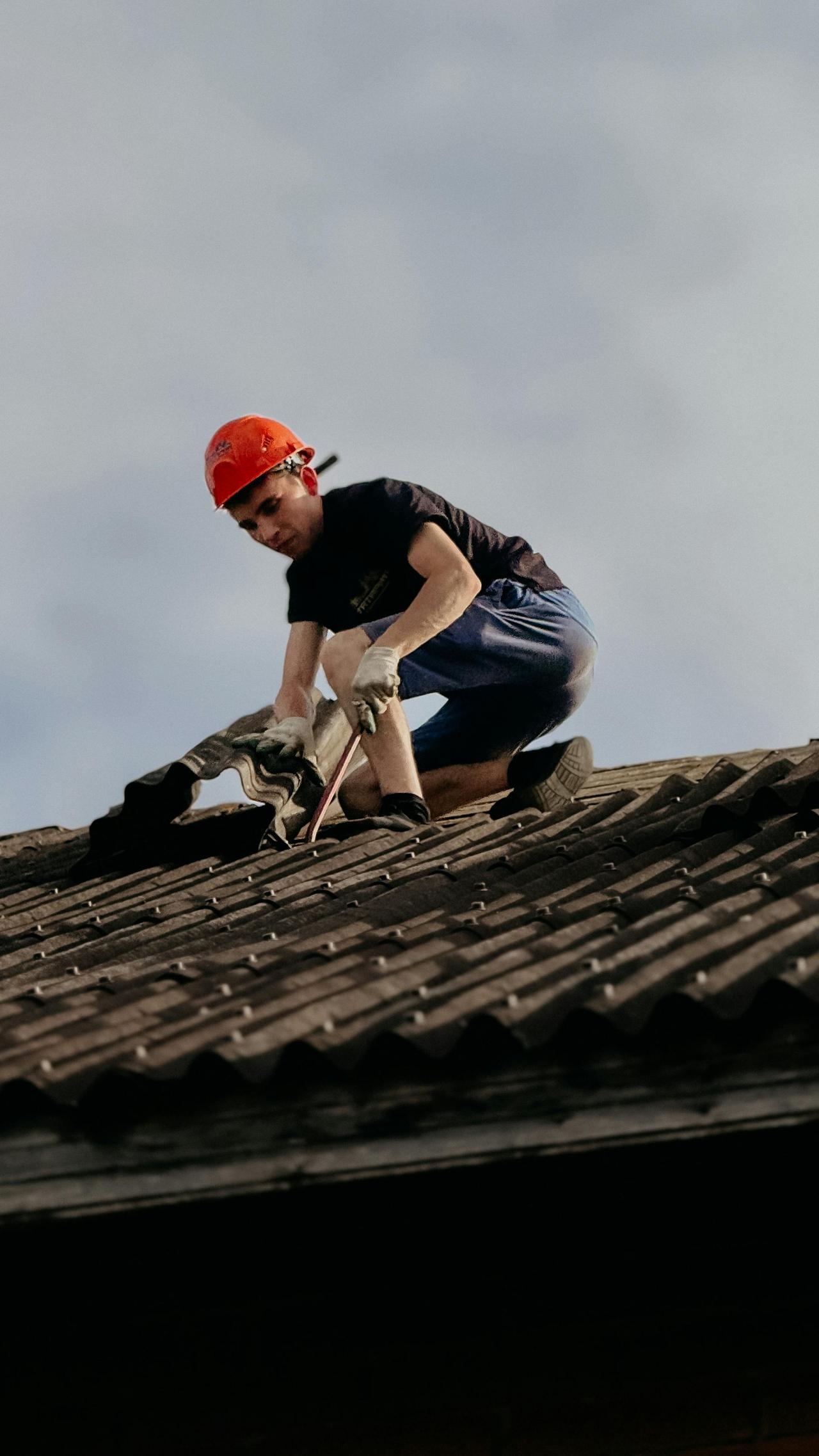 A construction worker with a safety helmet is repairing a roof outdoors during the day.