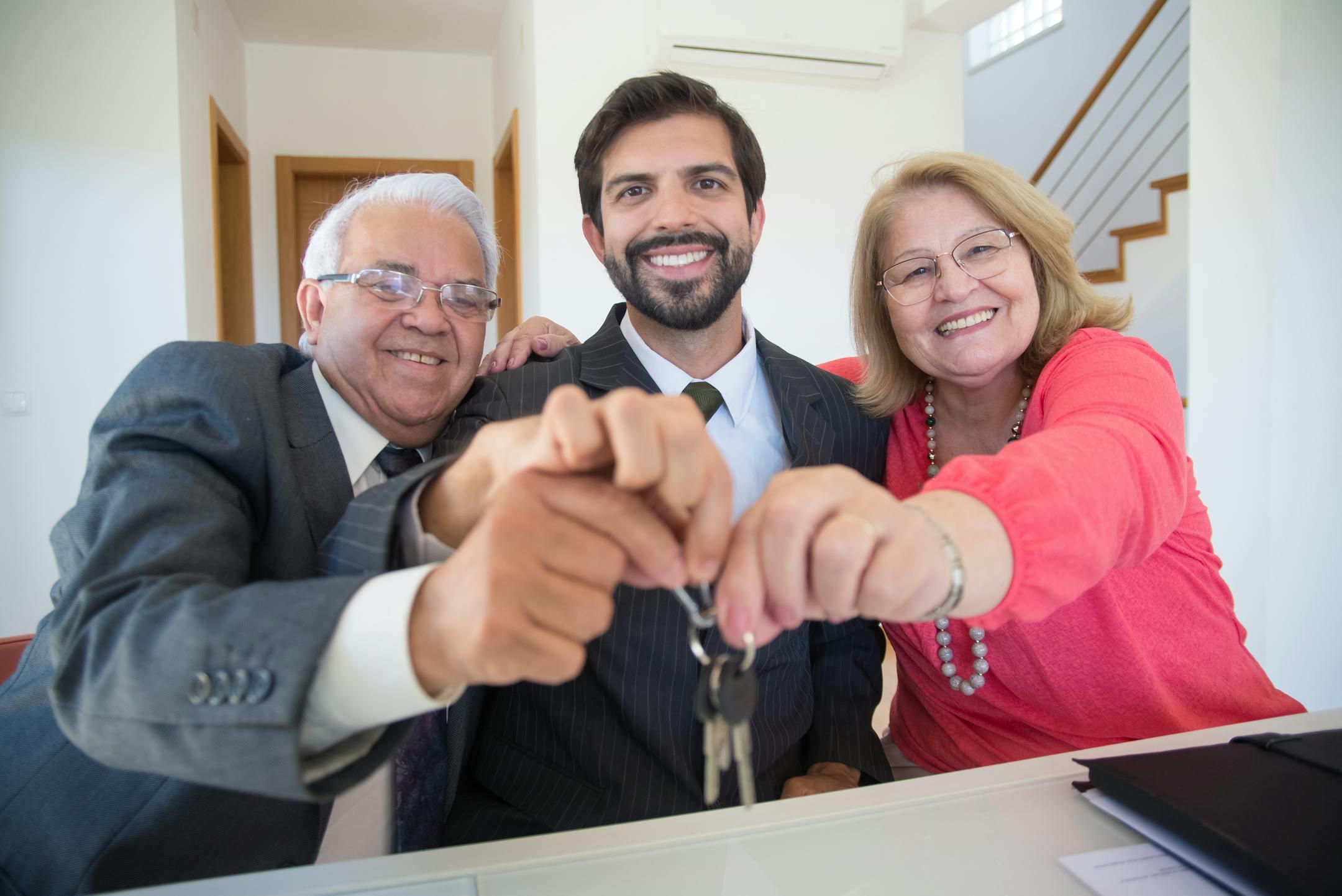 Smiling elderly couple receiving house keys from realtor indoors.