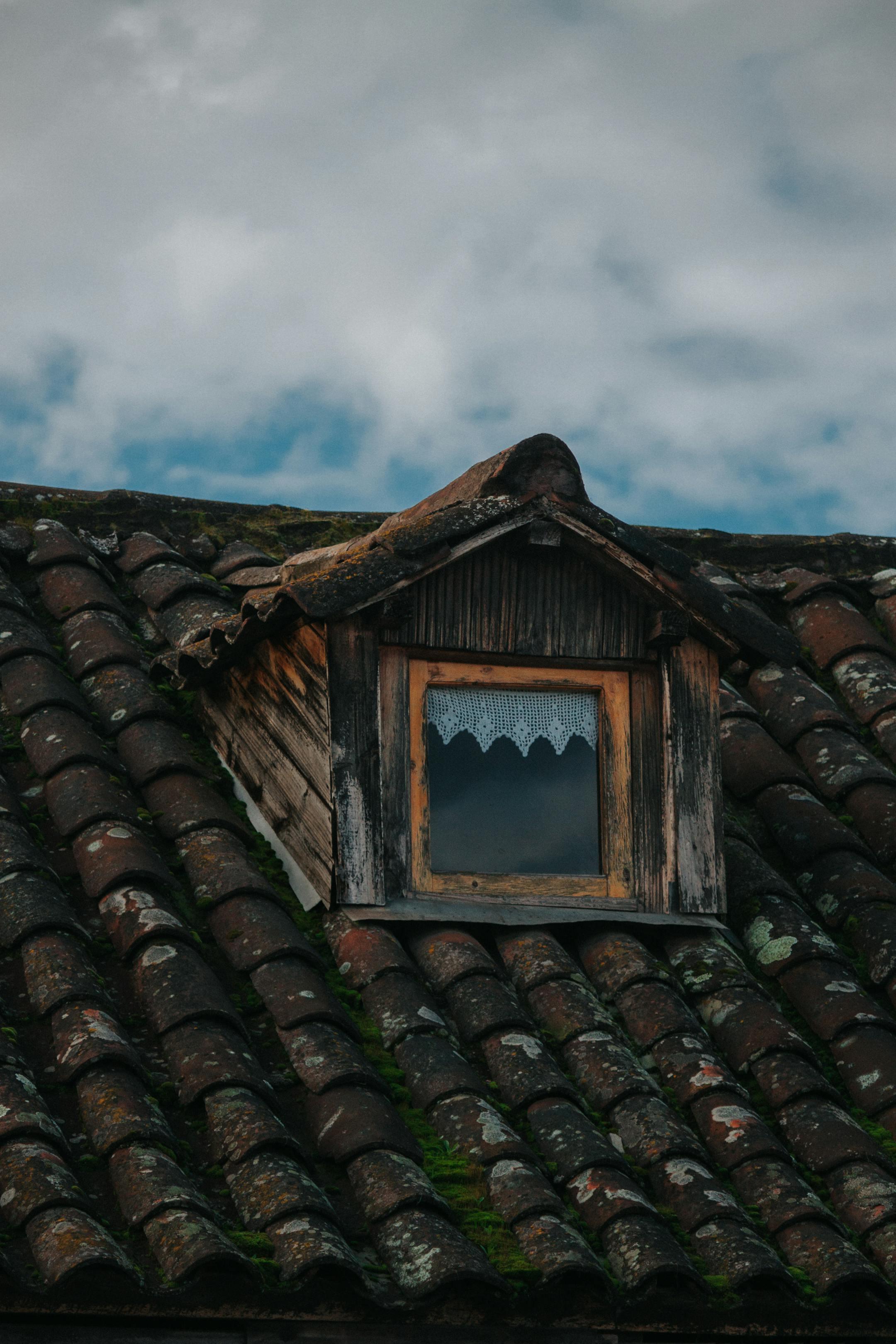 A close-up of a rustic wooden dormer window on a weathered tiled roof, showcasing aged architectural charm.