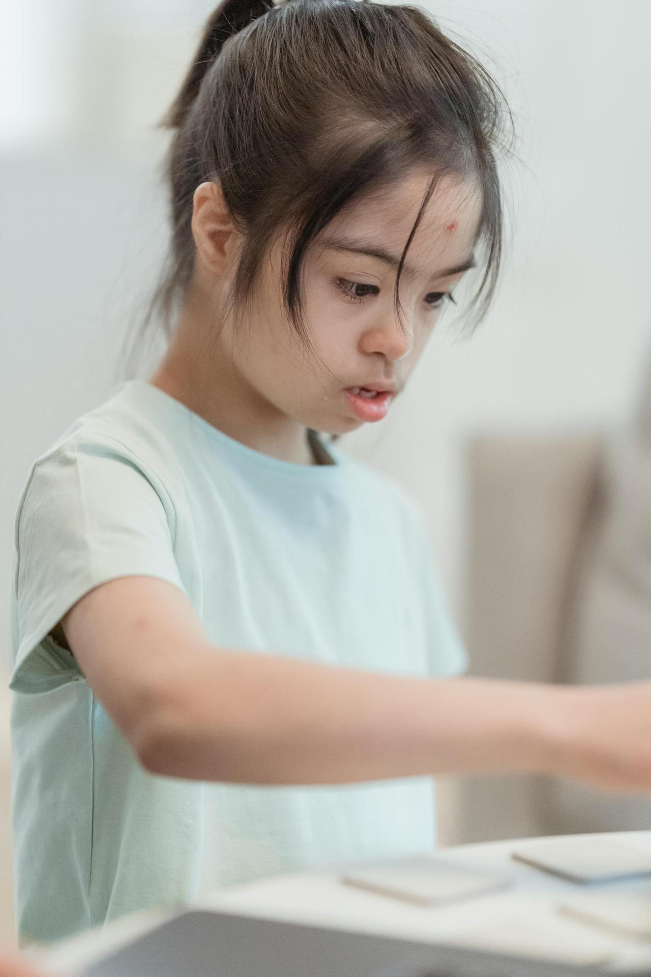Portrait of a focused young girl with Down syndrome looking intently at a task indoors.