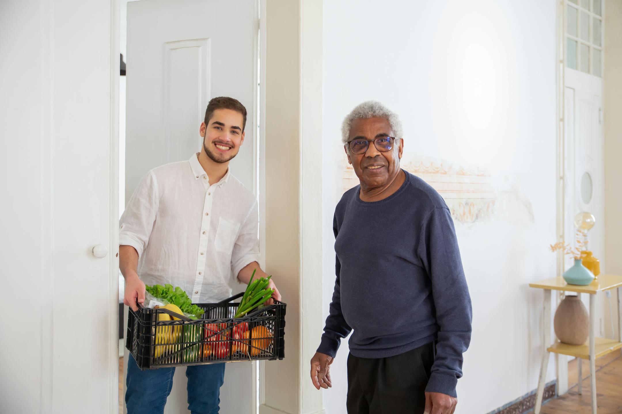 Senior man receiving fresh produce from a young volunteer indoors, promoting community support.