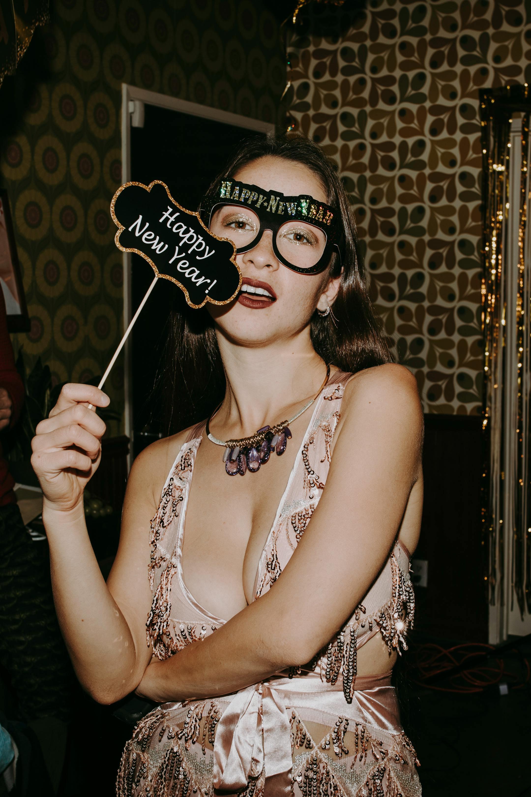 A young woman celebrating New Year's Eve with festive glasses and a Happy New Year sign.