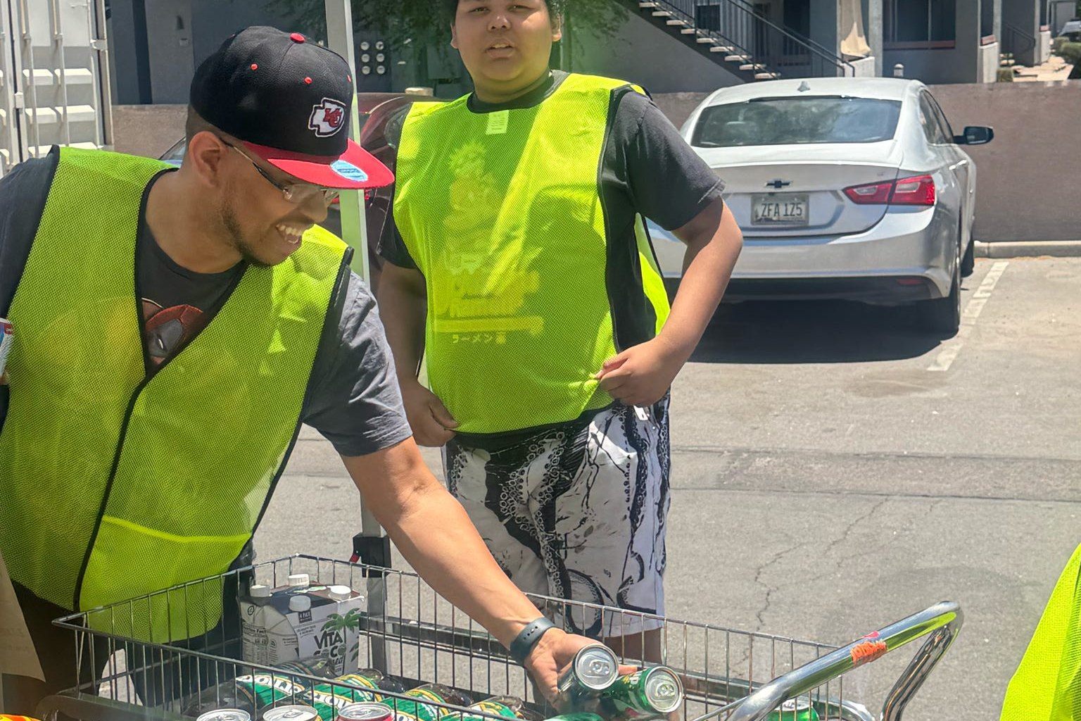 Two participants in safety vests loading groceries into a cart together outside the center.