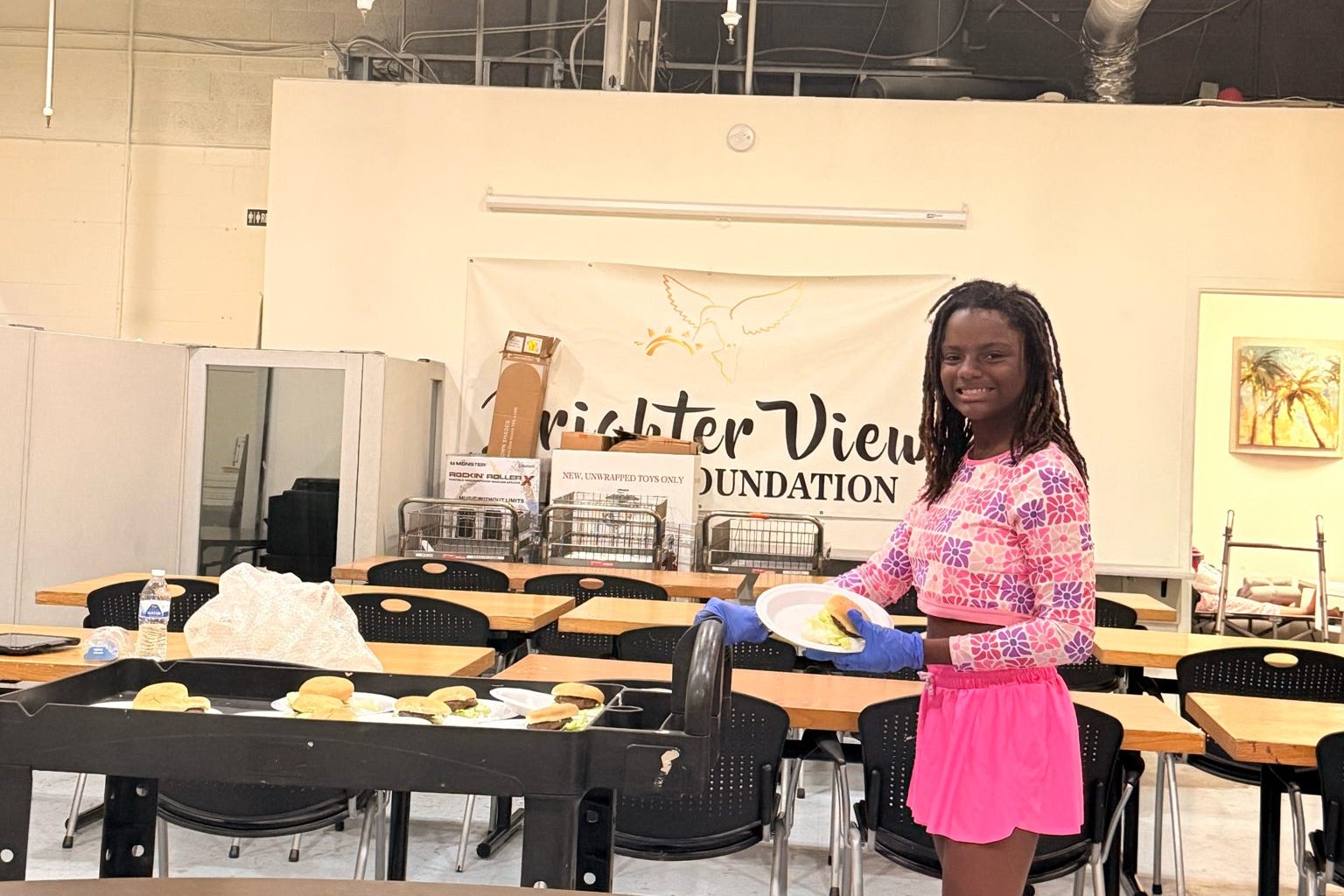 A Brighter View team member serving plated meals beside the Brighter View Foundation banner.