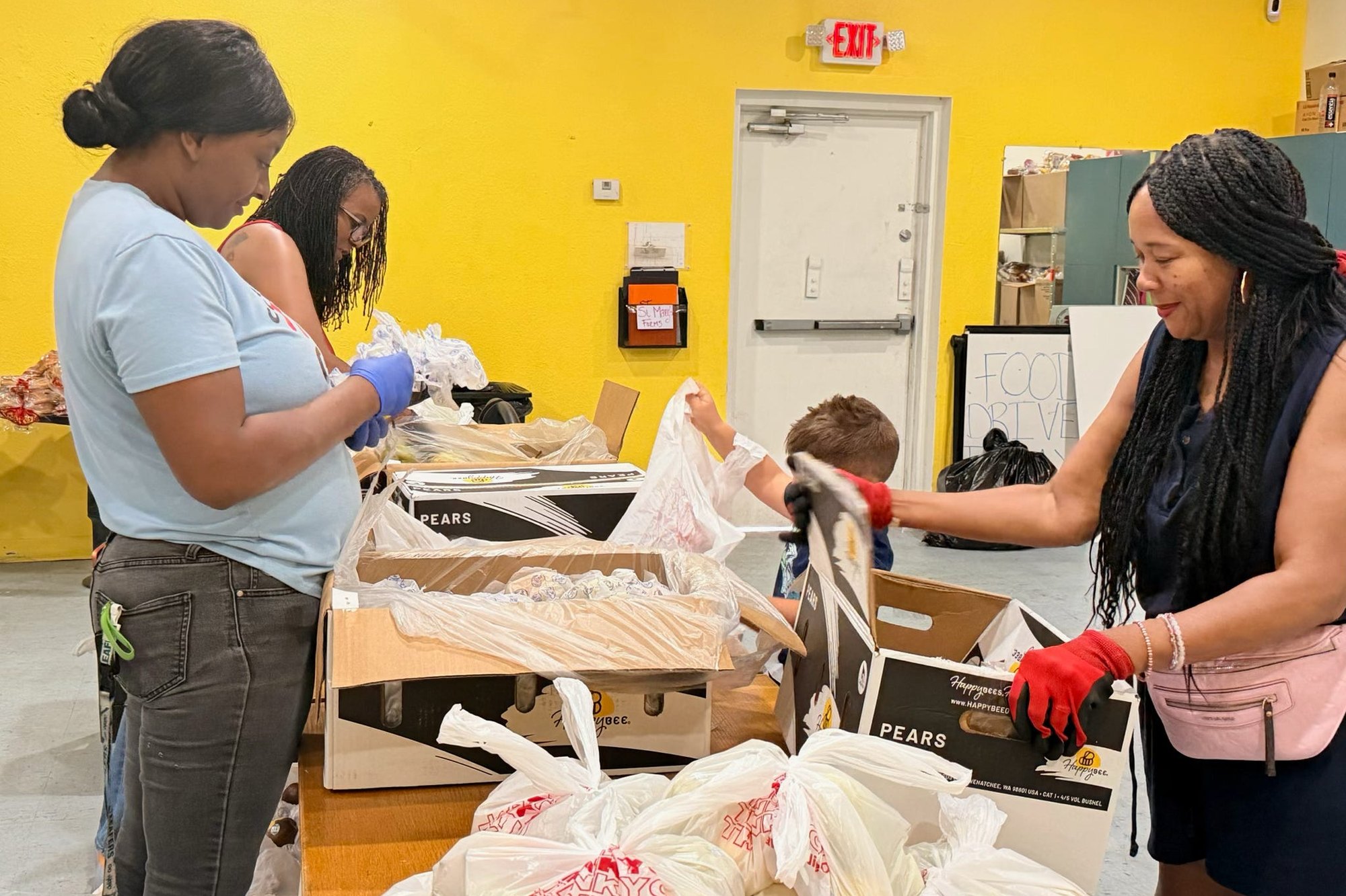 Volunteers in gloves bagging fresh produce into boxes at the pantry.